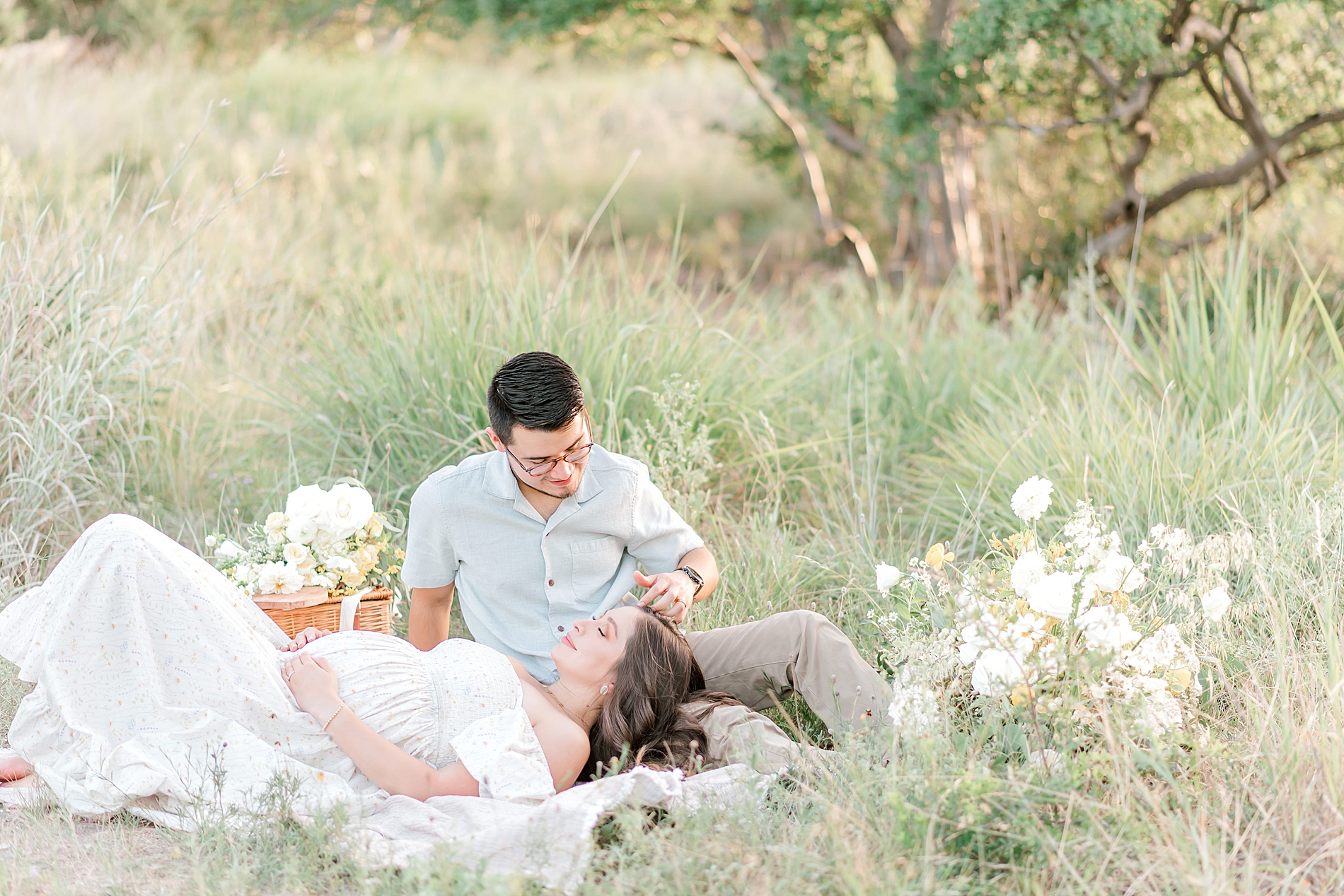 woman lays down in grass with husband during maternity session