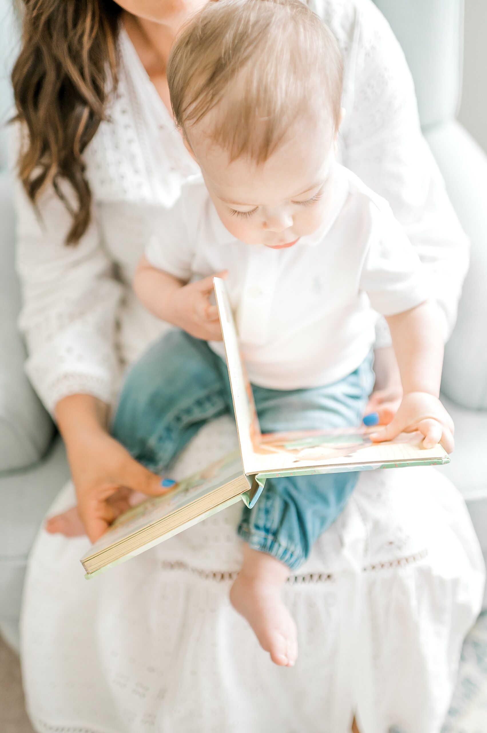 candid photo of little boy reading book in mom's lap