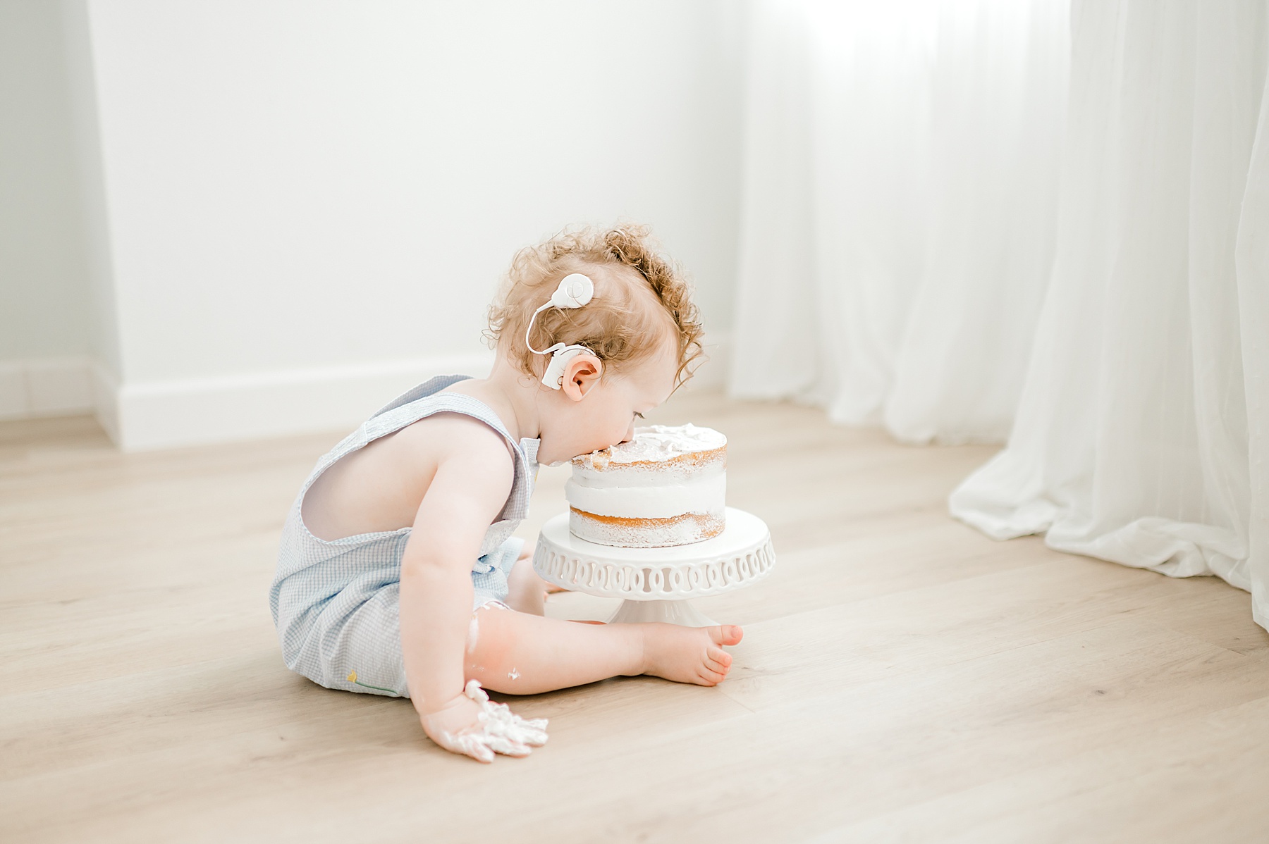 little boy leans over to eat white cake