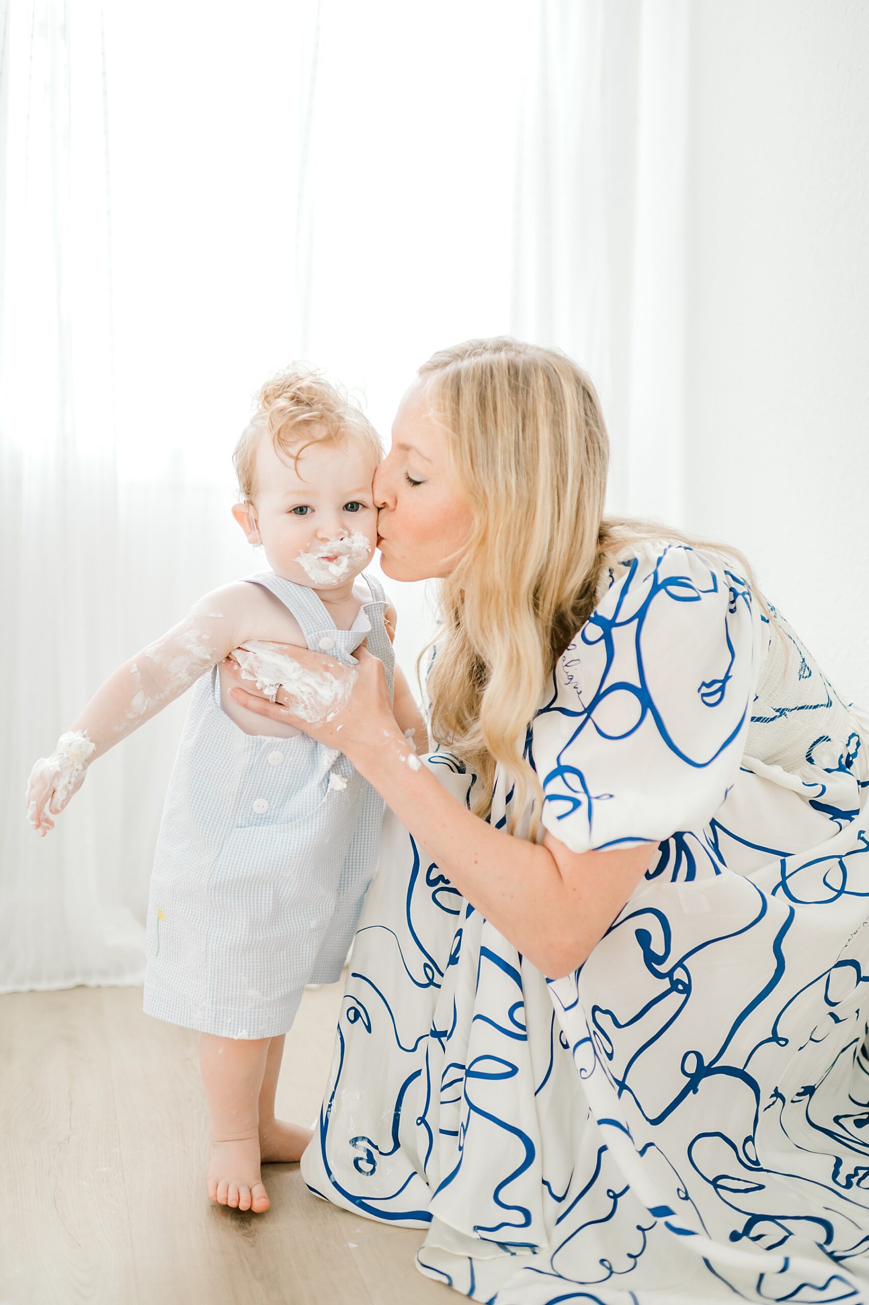 mom kisses little boy covered in cake during One Year Milestone Studio Session