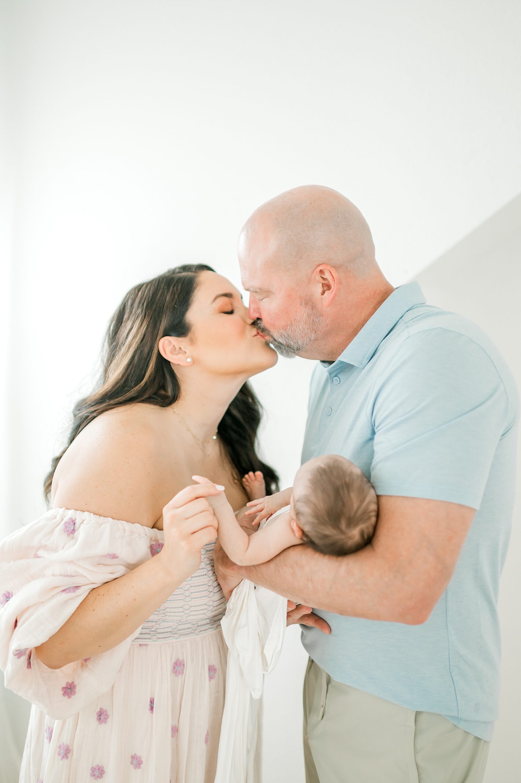 parents kiss as they hold their newborn girl