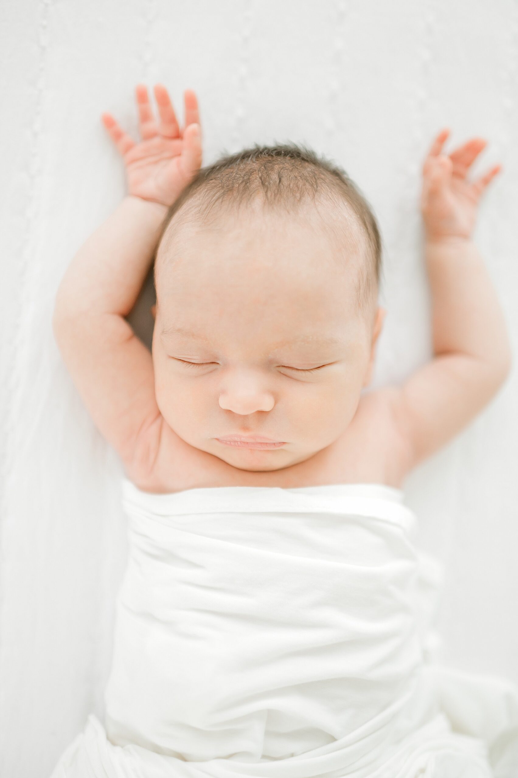 newborn sleeps while swaddled in white blanket 