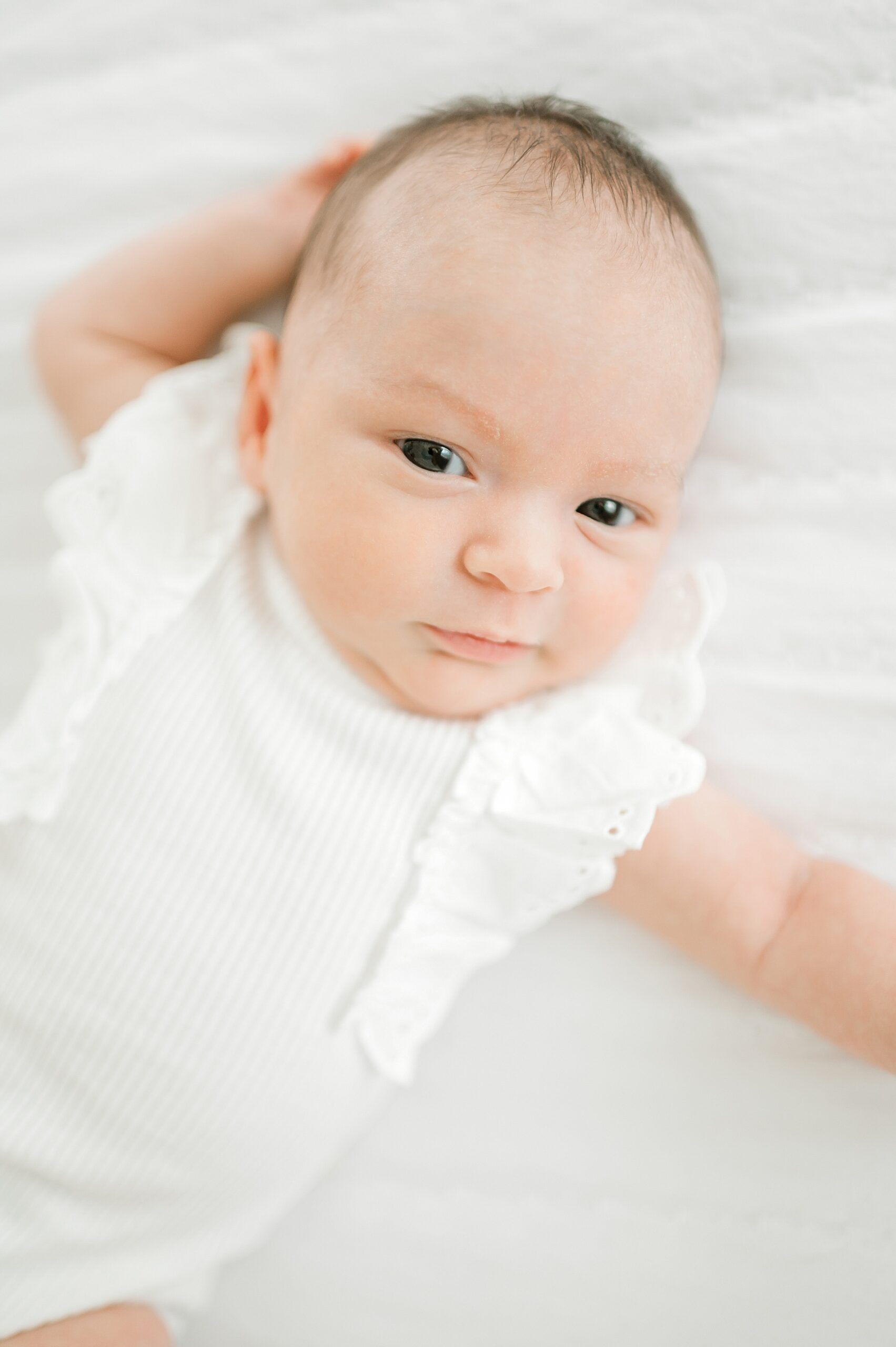 wide-eyed newborn in white outfit