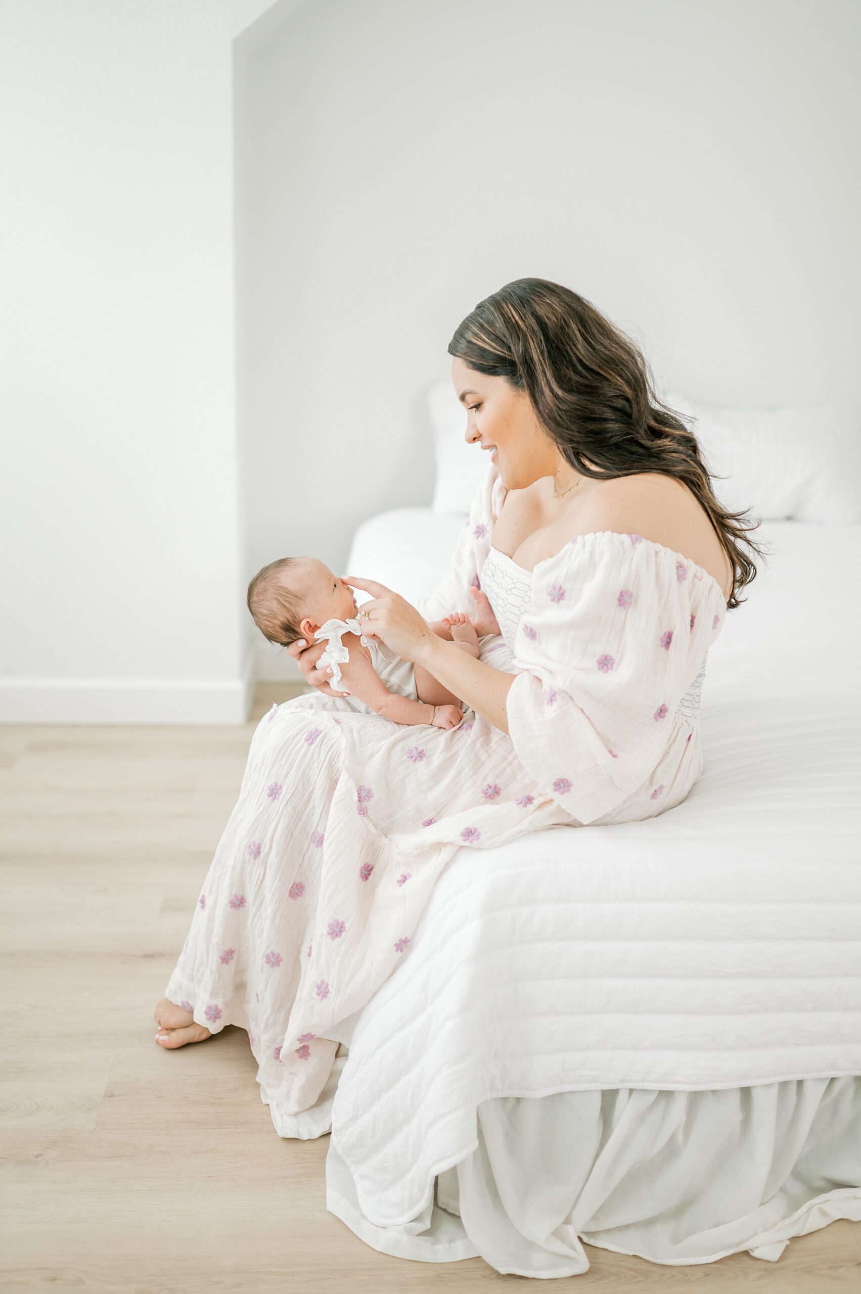 mom holds sweet newborn while sitting on white bed