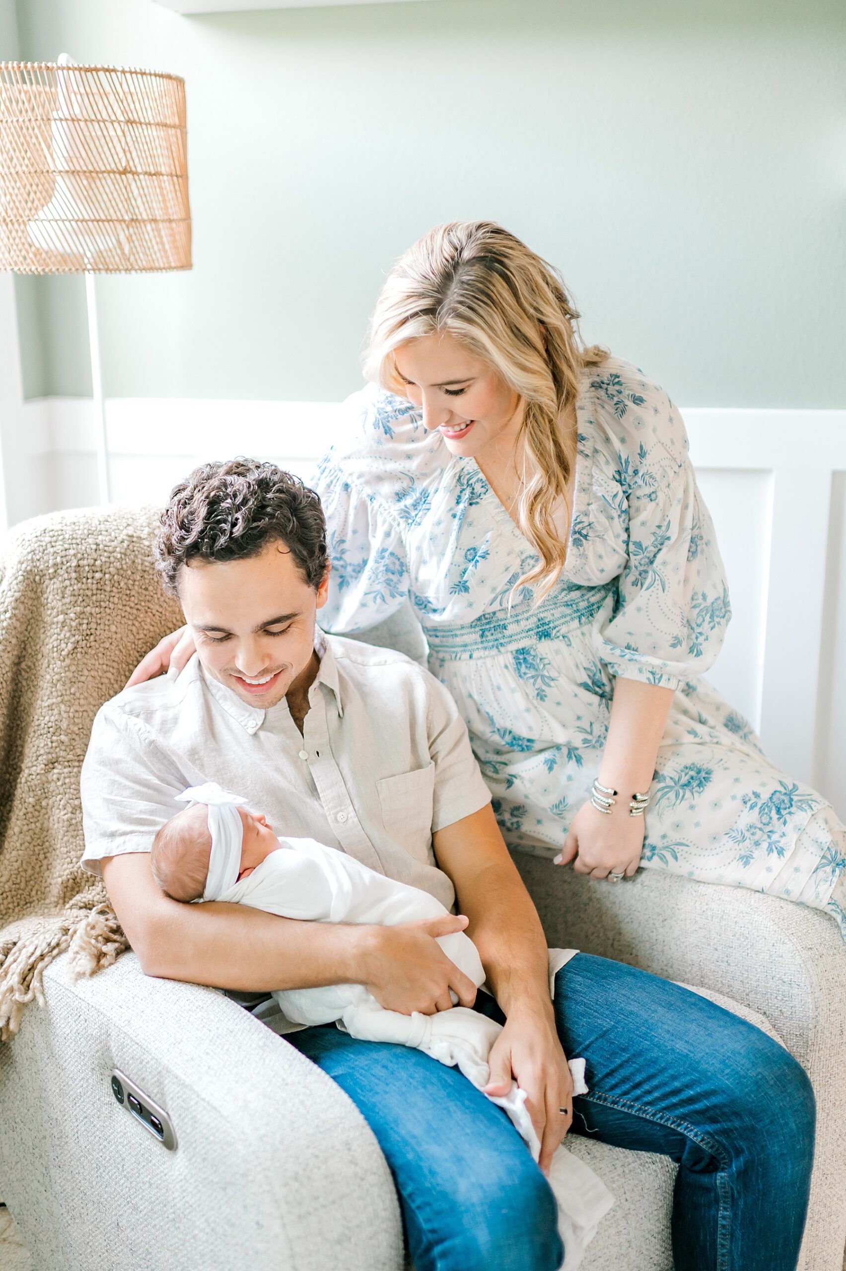 parents hold newborn in cozy chair in nursery