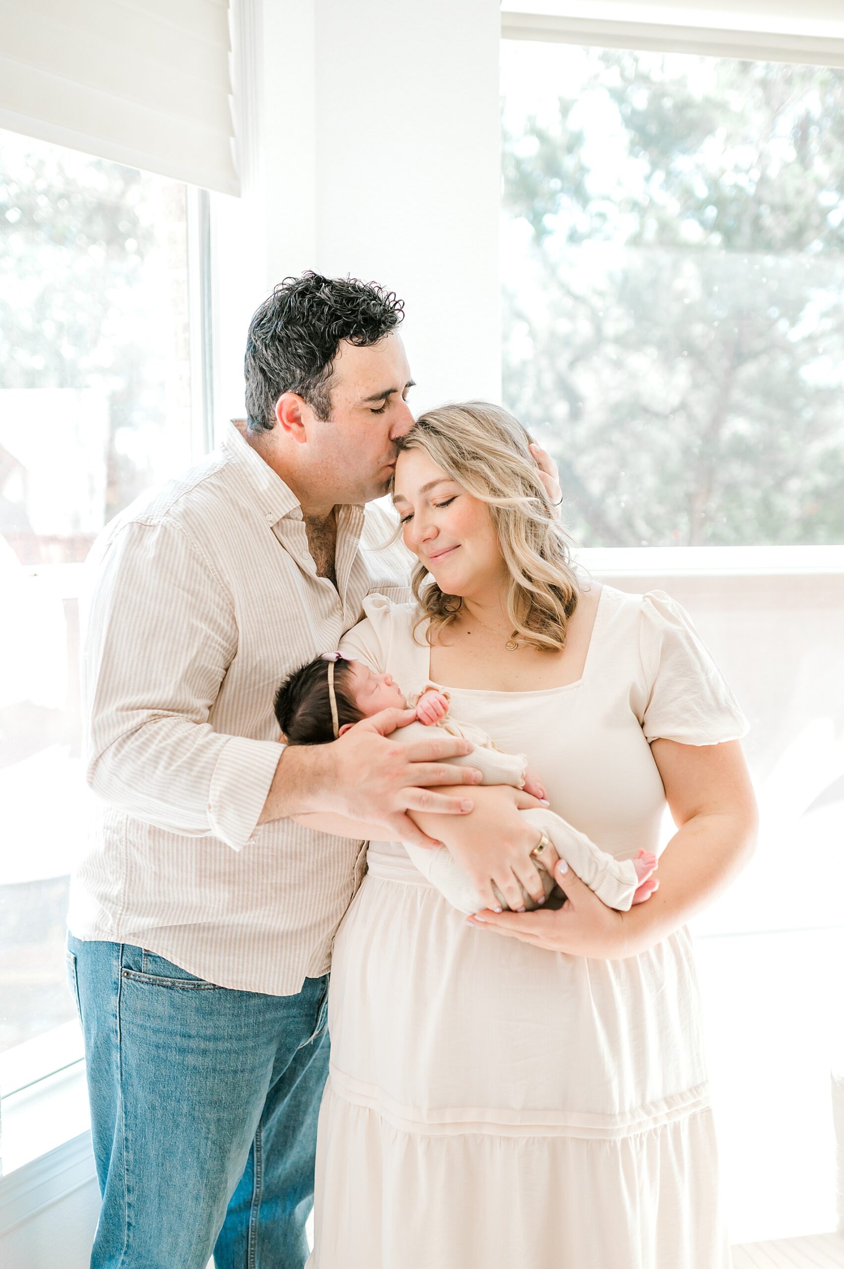 parents hold newborn girl as dad kisses mom's head