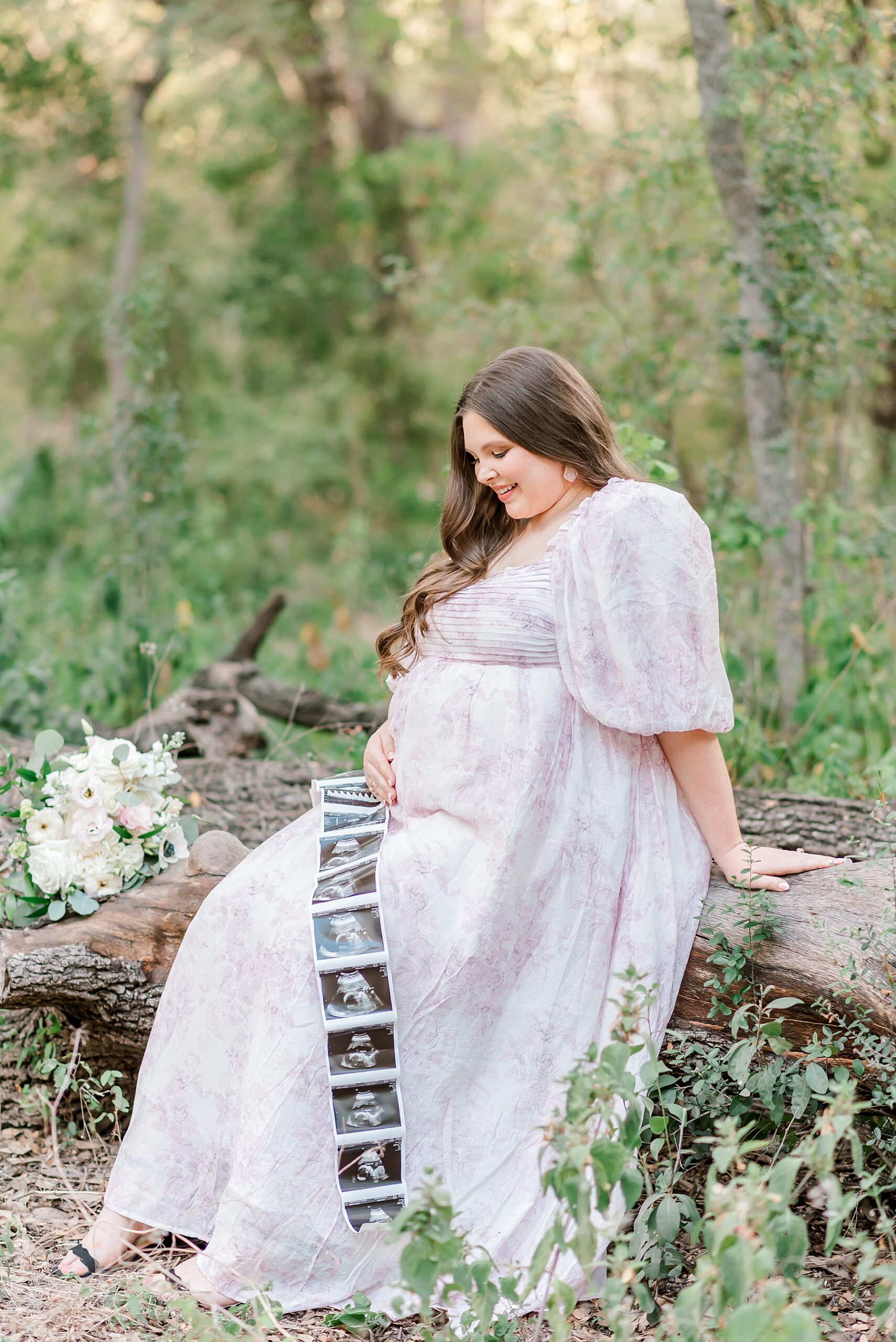 expectant mother sits and holds baby bump while looking at sonogram photos