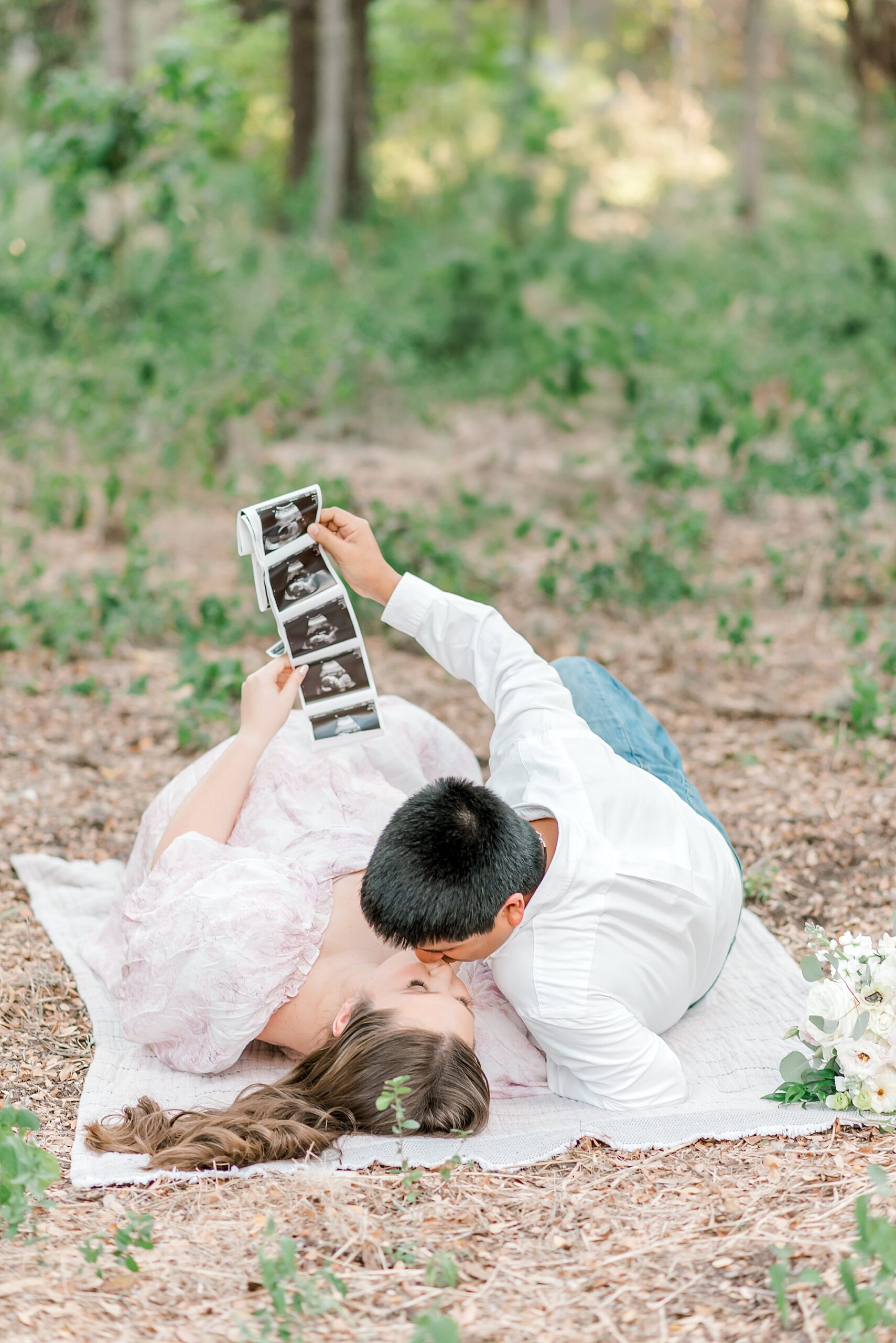 couple lay on blanket holding sonogram 