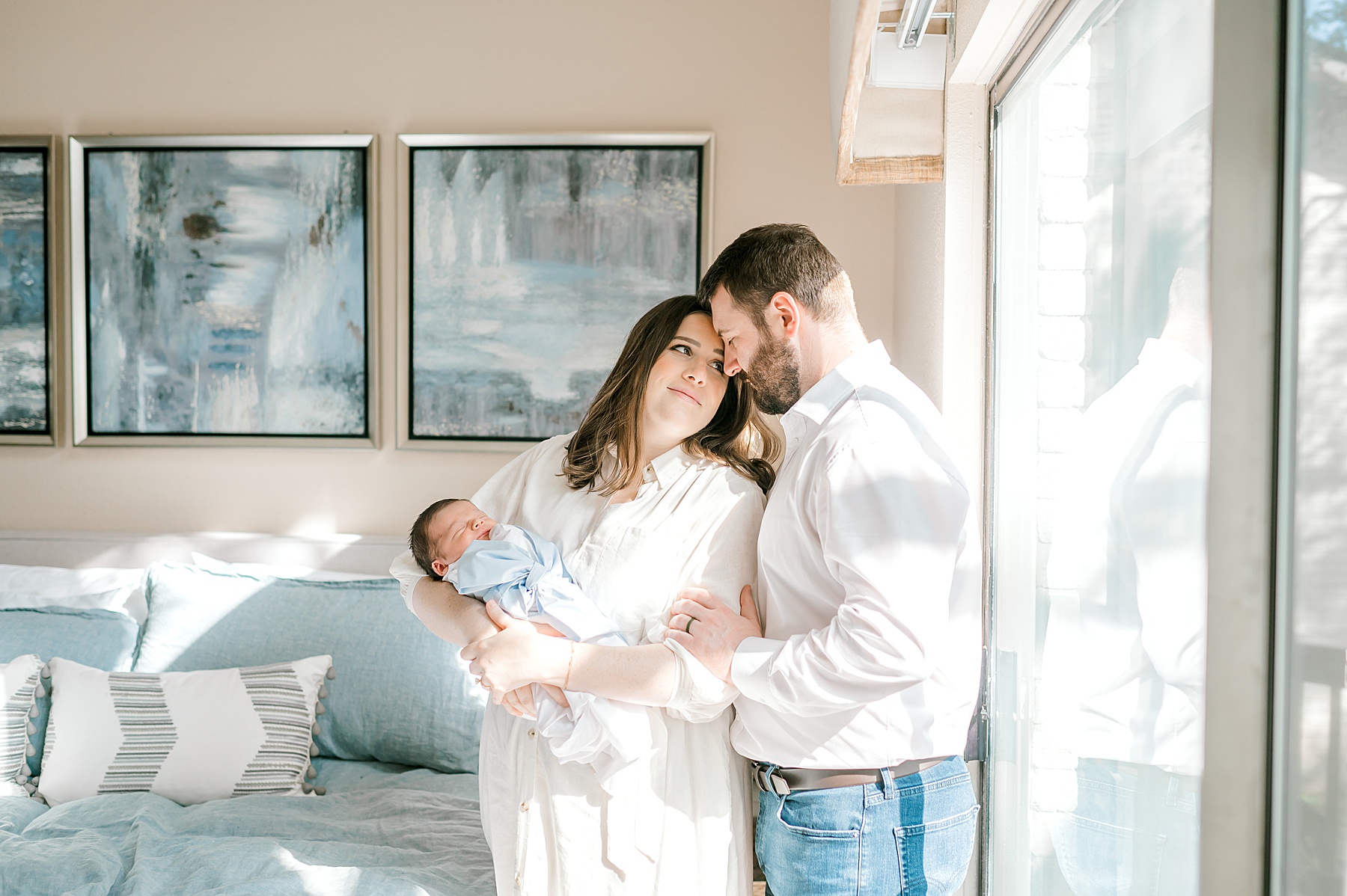 parents hold newborn by window 