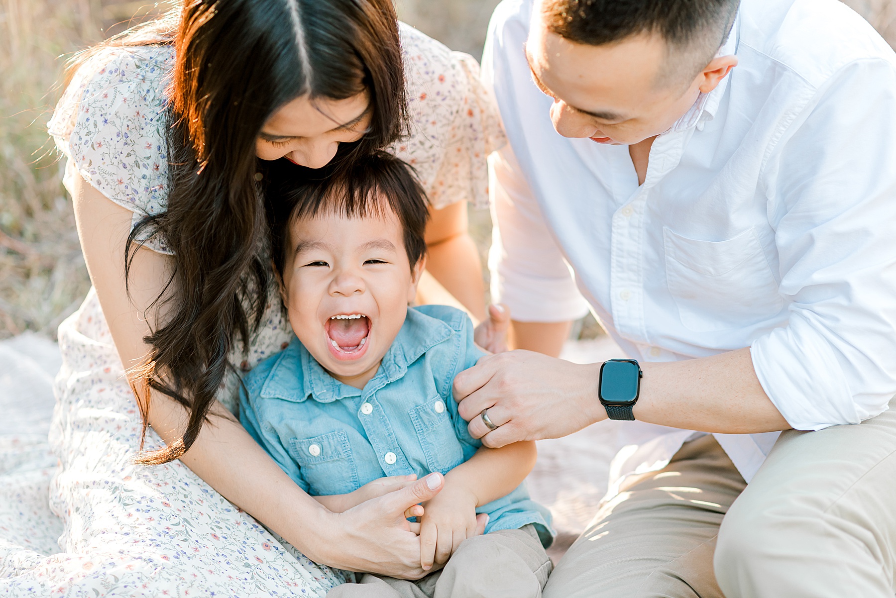 parents tickle their son as he laughs