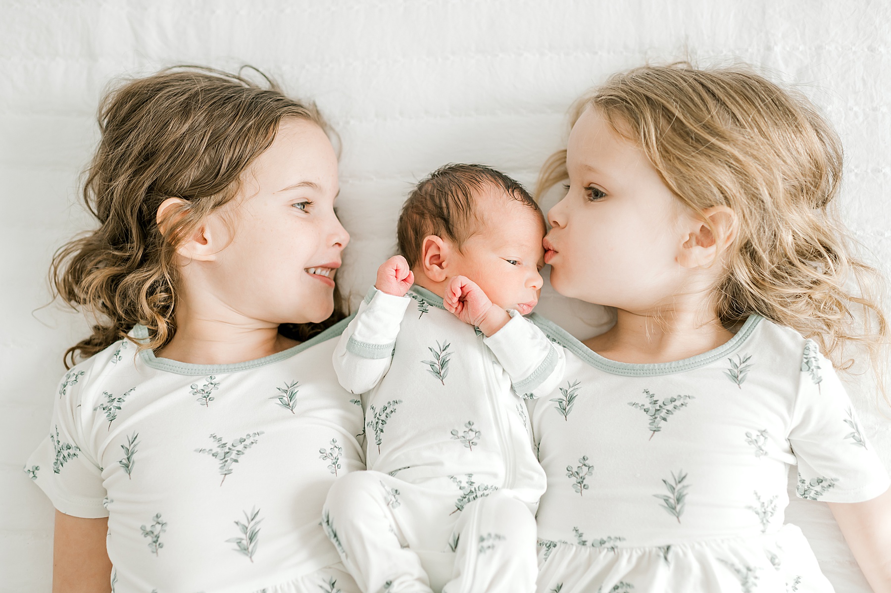 big sisters snuggle with newborn brother