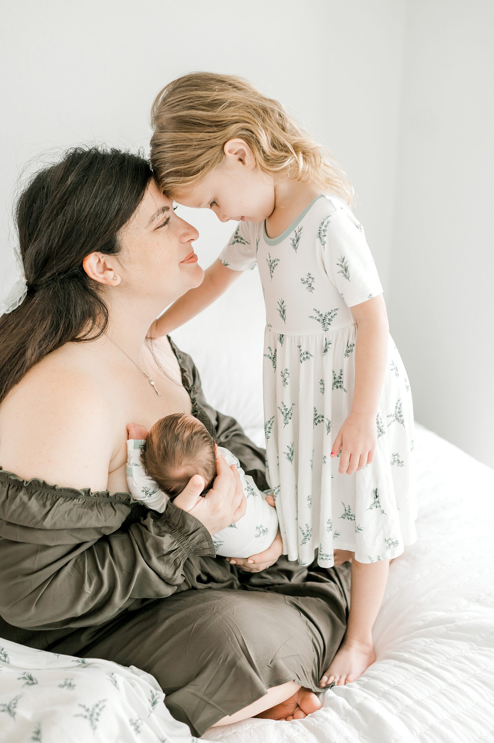 mom holds newborn while daughter looks down at her baby brother