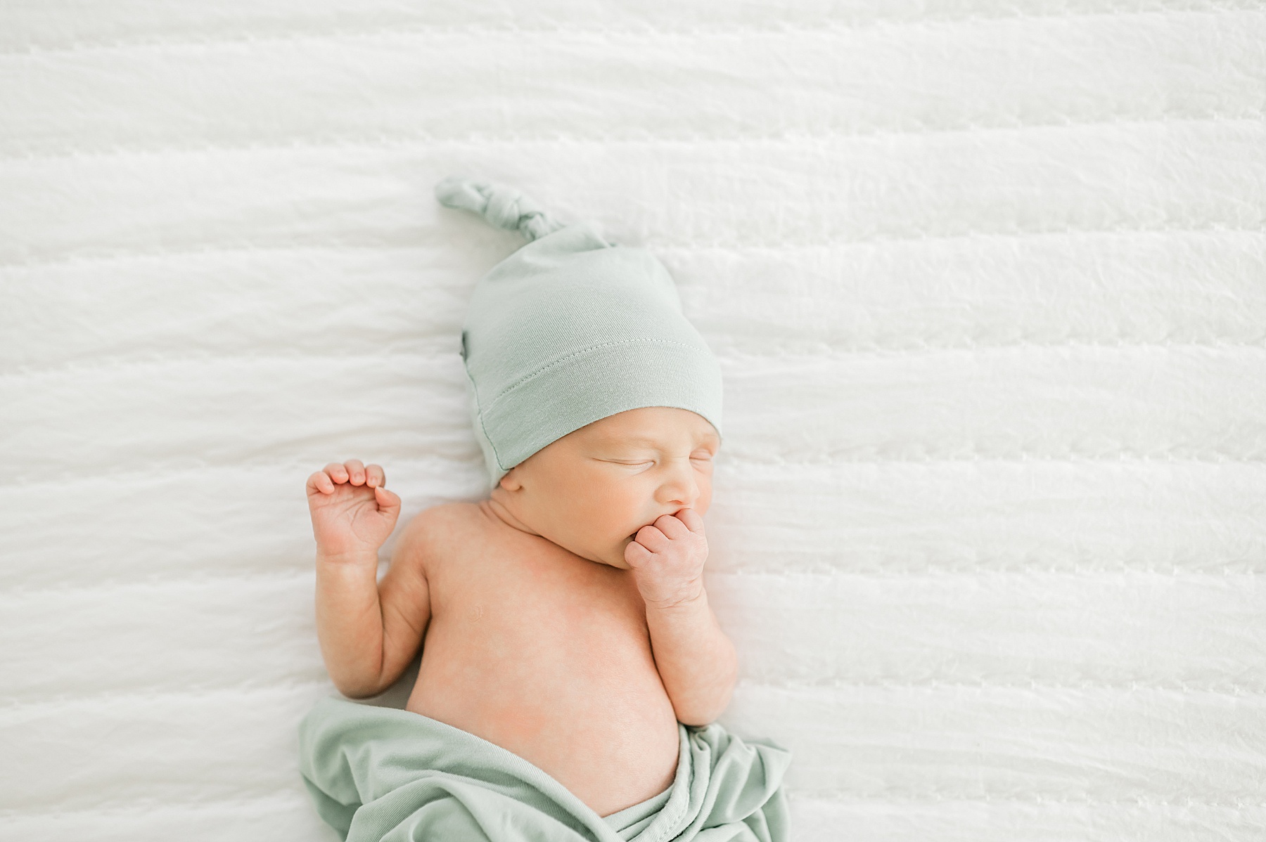 newborn boy in sage green hat and blanket