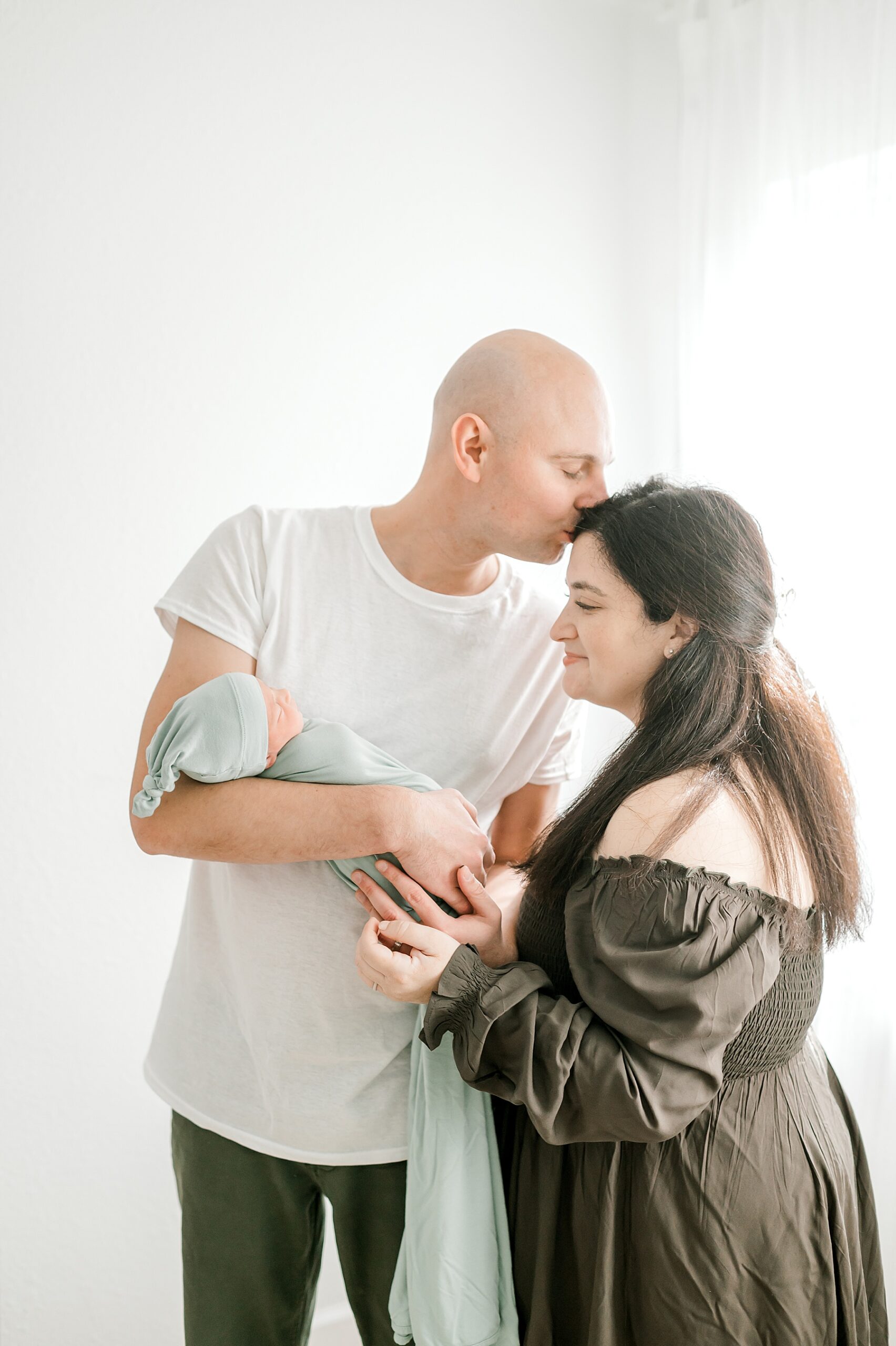 parents hold newborn boy swaddled in sage green blanket