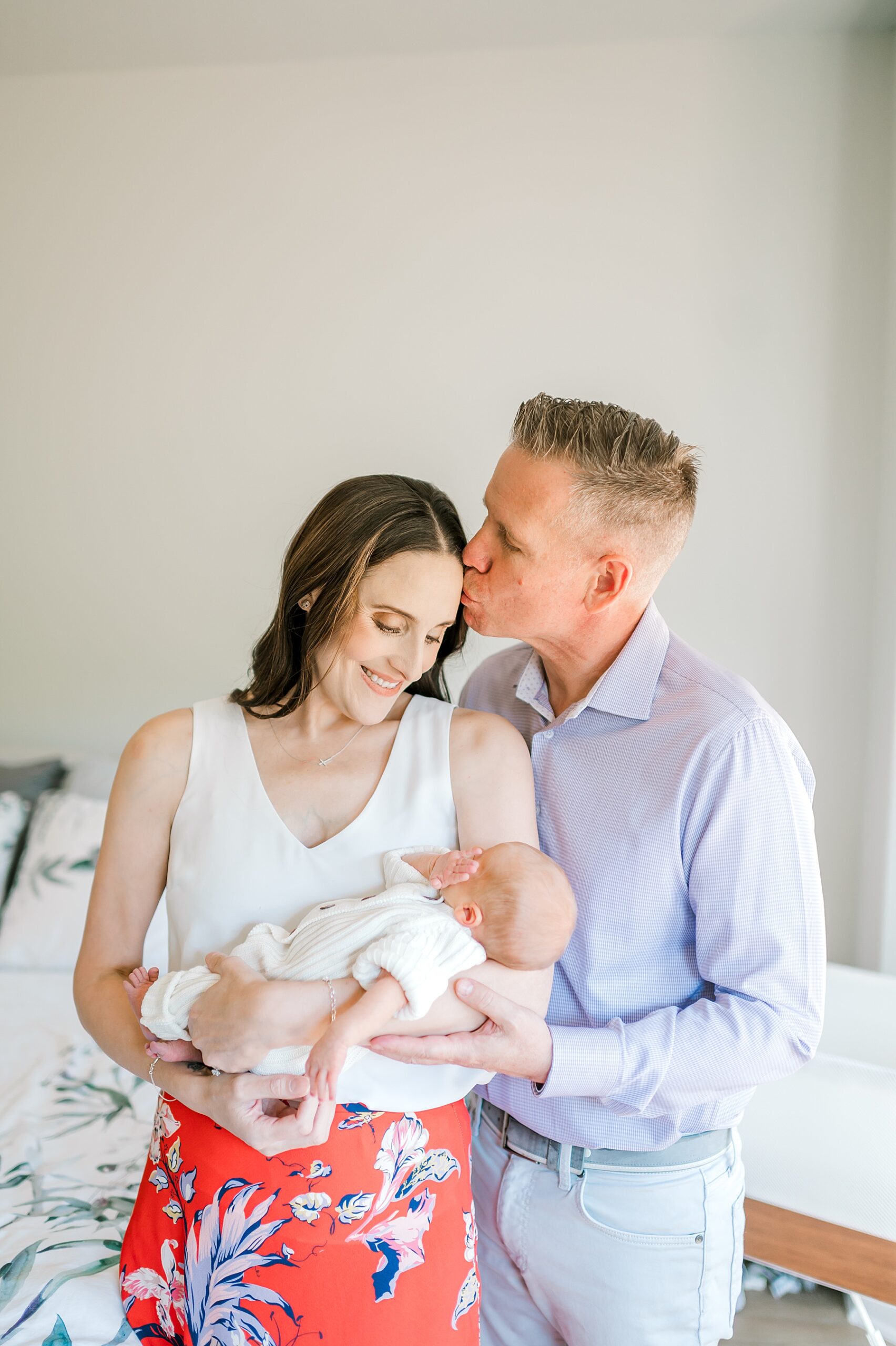 husband kisses his wife while holding their newborn boy