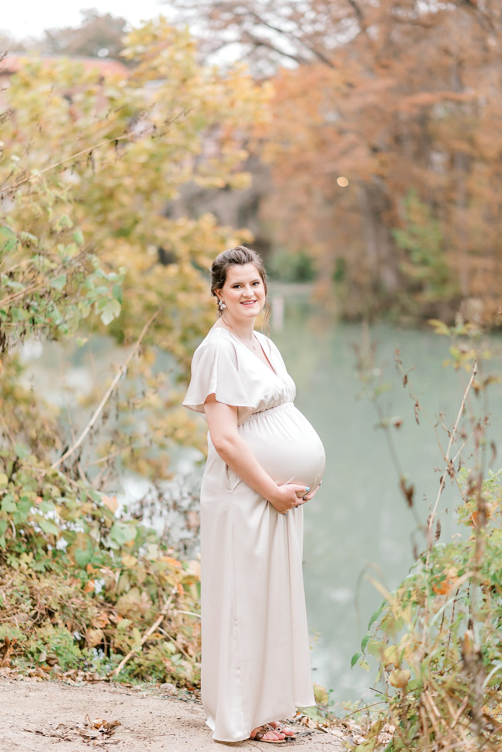 expecting mom holds belly by the water in Max Starcke Park