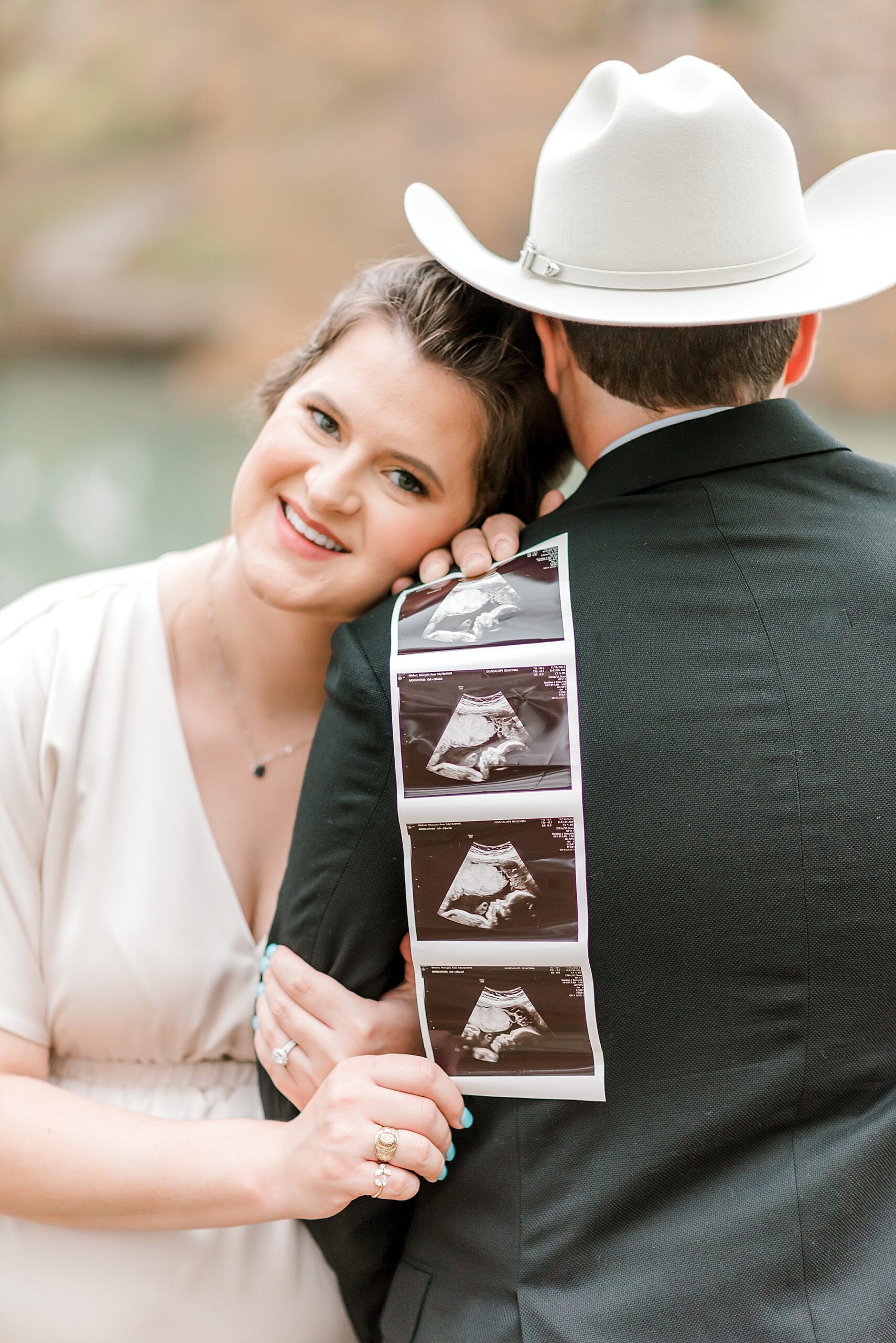 woman holds ultrasound photos of baby over husband's shoulder 