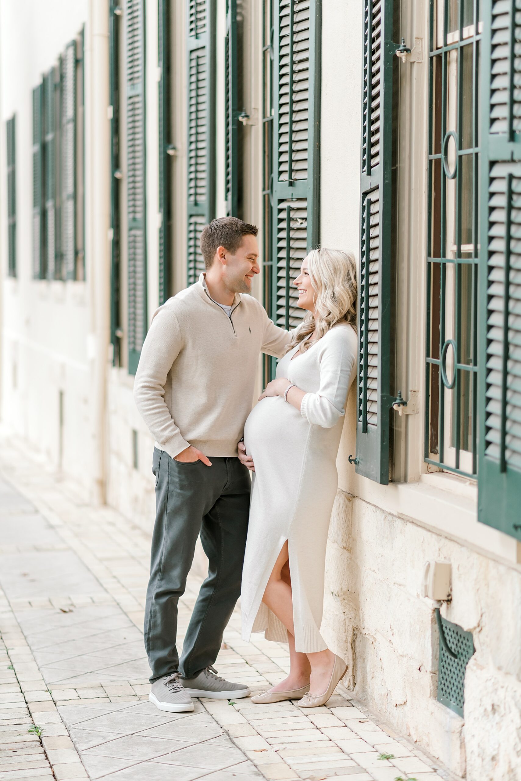 pregnant woman leans against building with her husband 