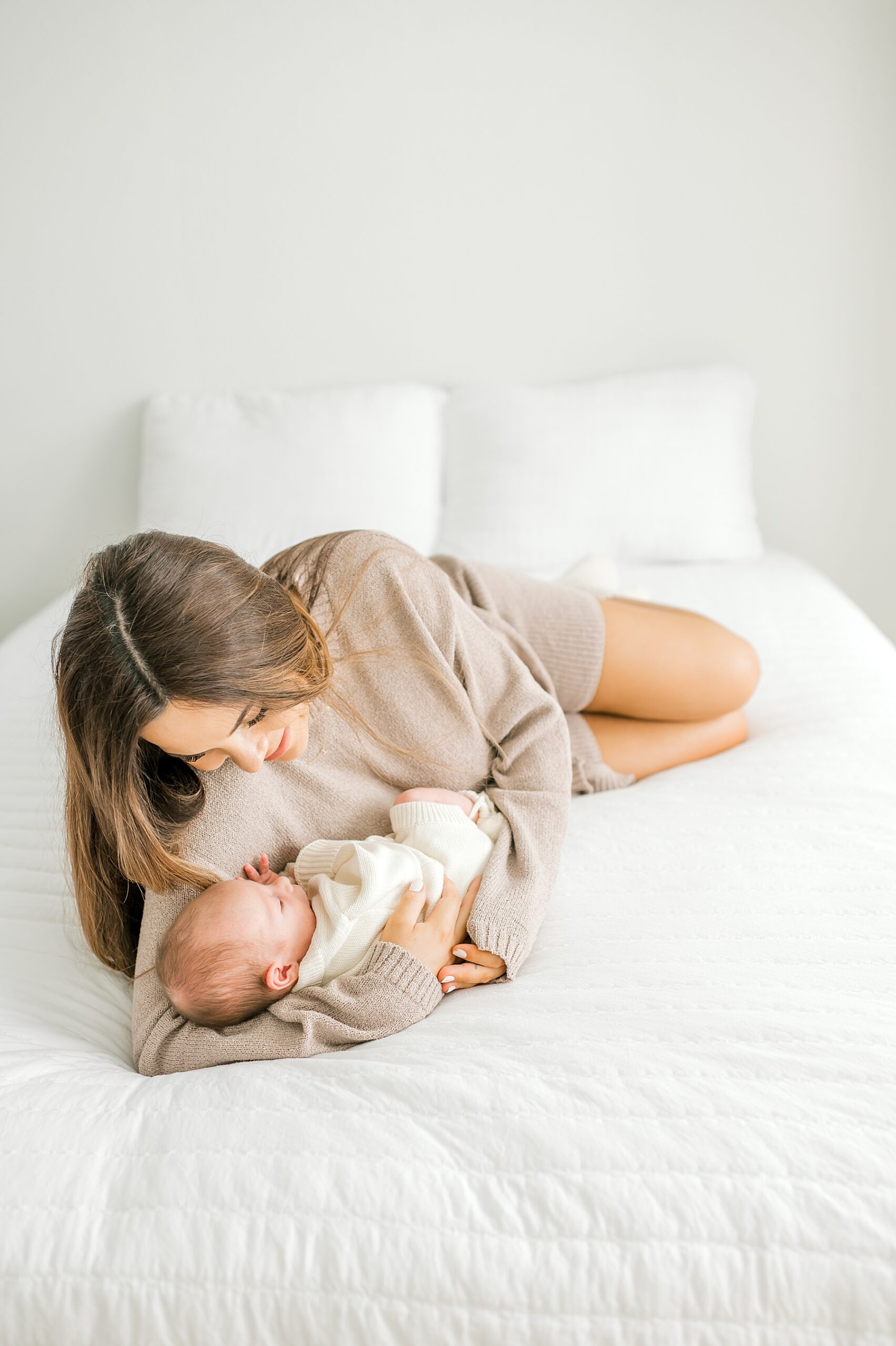 mom in cozy sweater snuggles newborn on bed