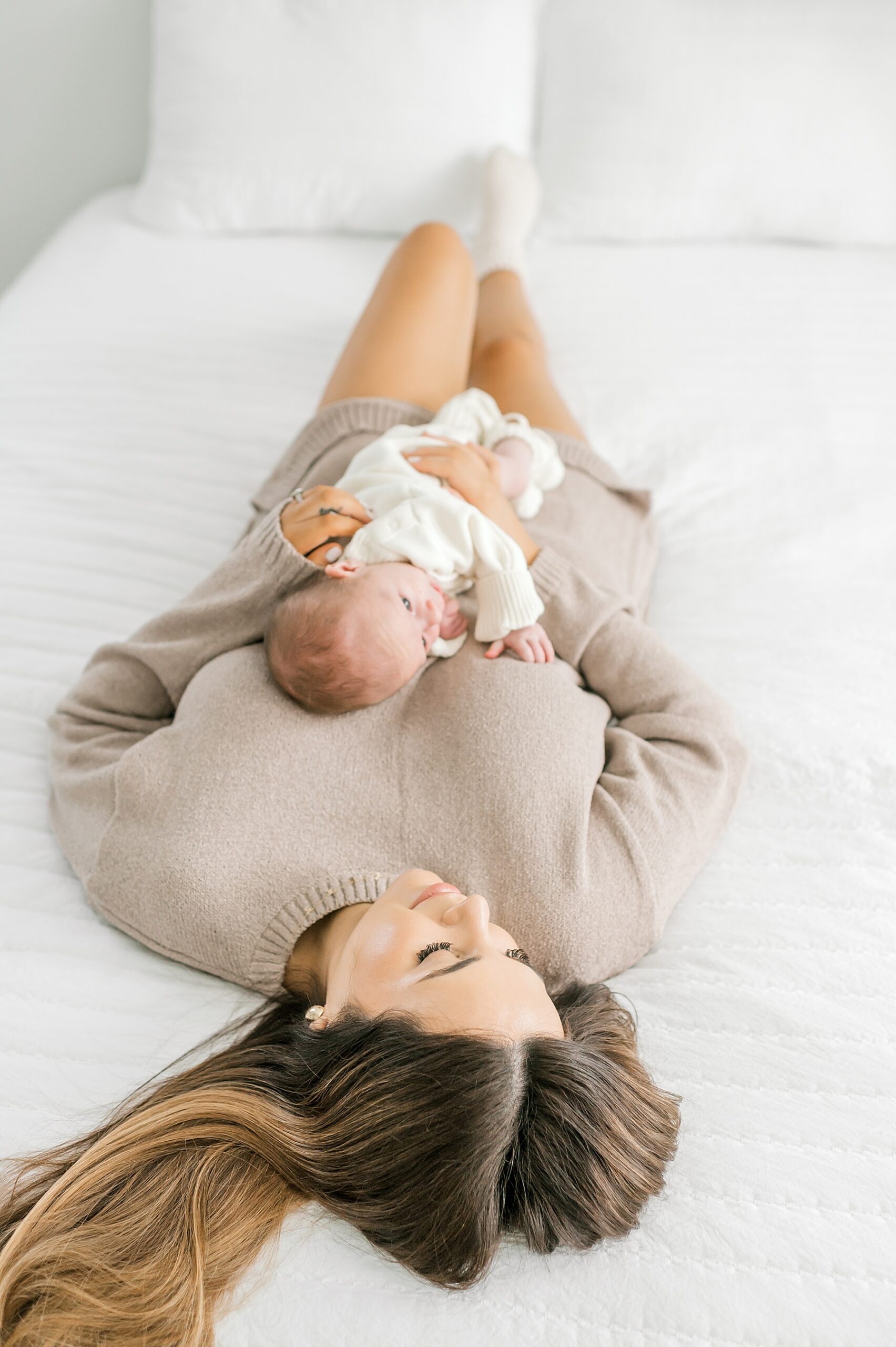 mom lays on bed with newborn on chest during cozy studio newborn session