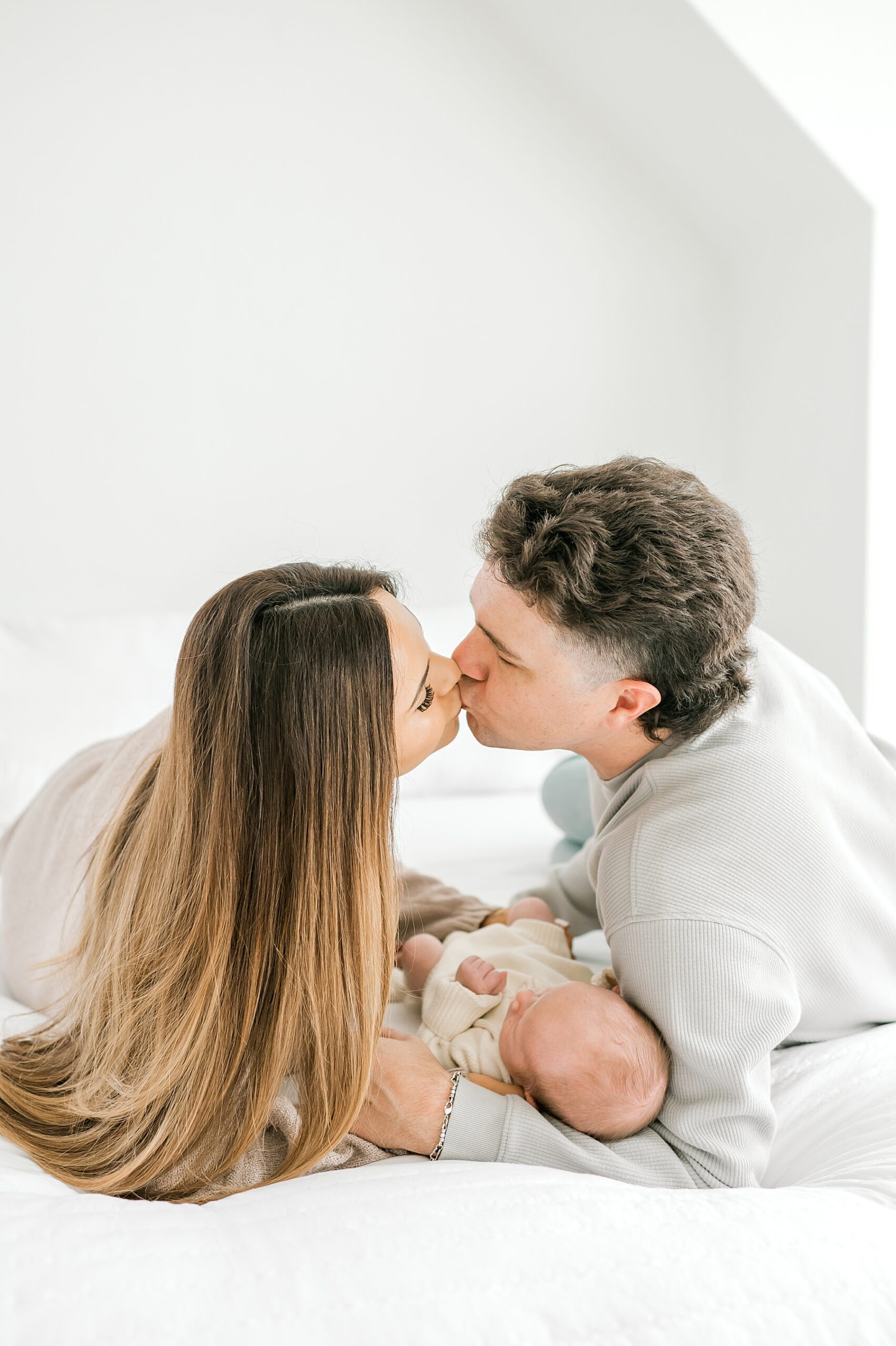 parents kiss as they hold newborn during Cozy Newborn Session in Bulverde, Texas