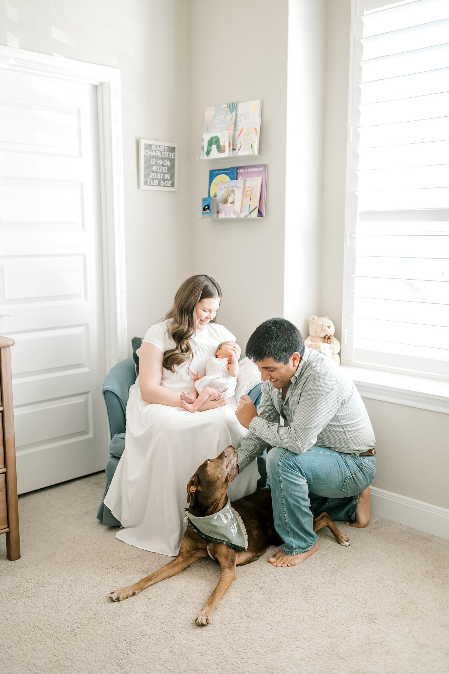 parents hold newborn in rocking chair with family dog nearby
