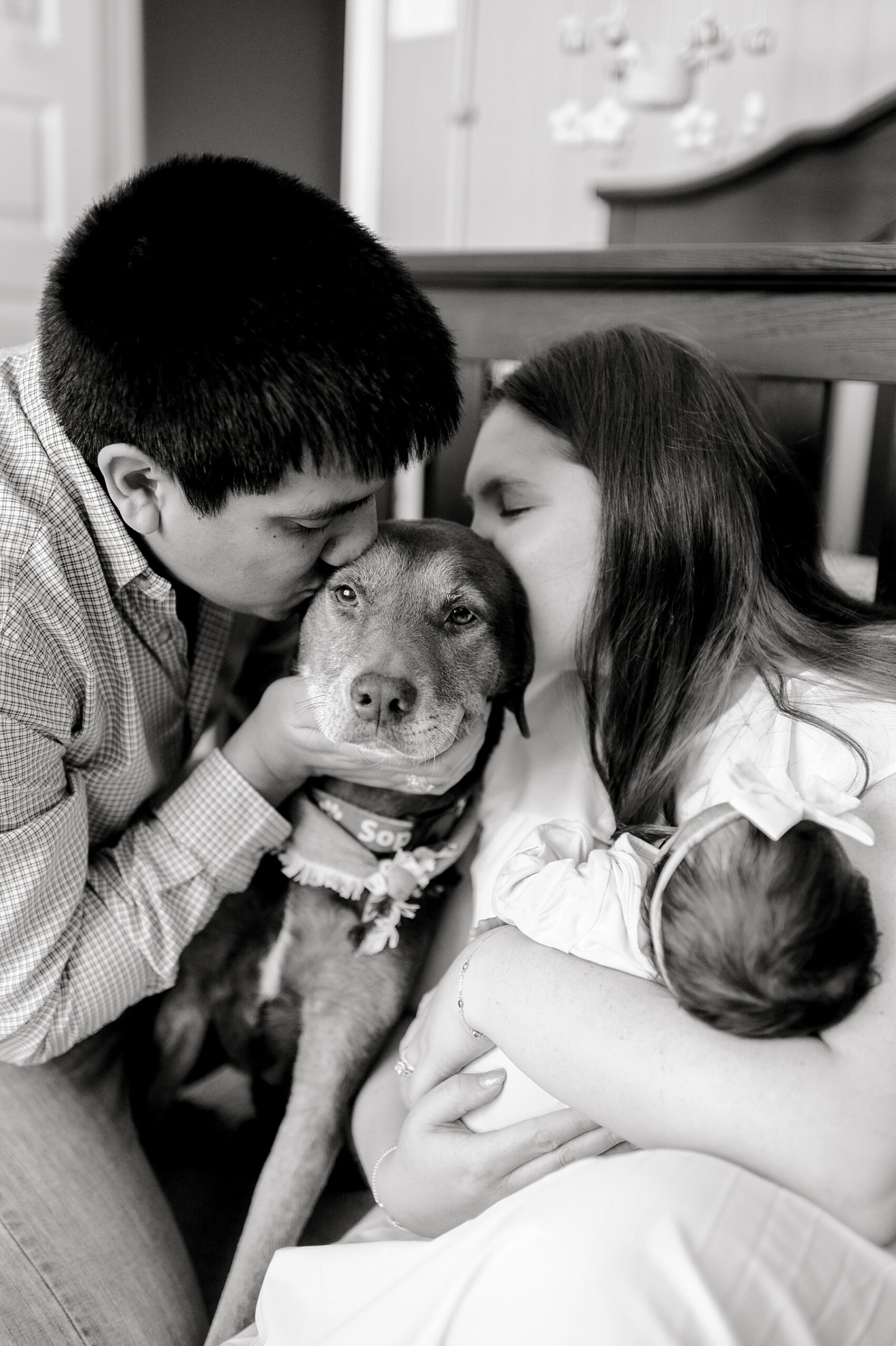 parents kiss their dog while holding newborn girl