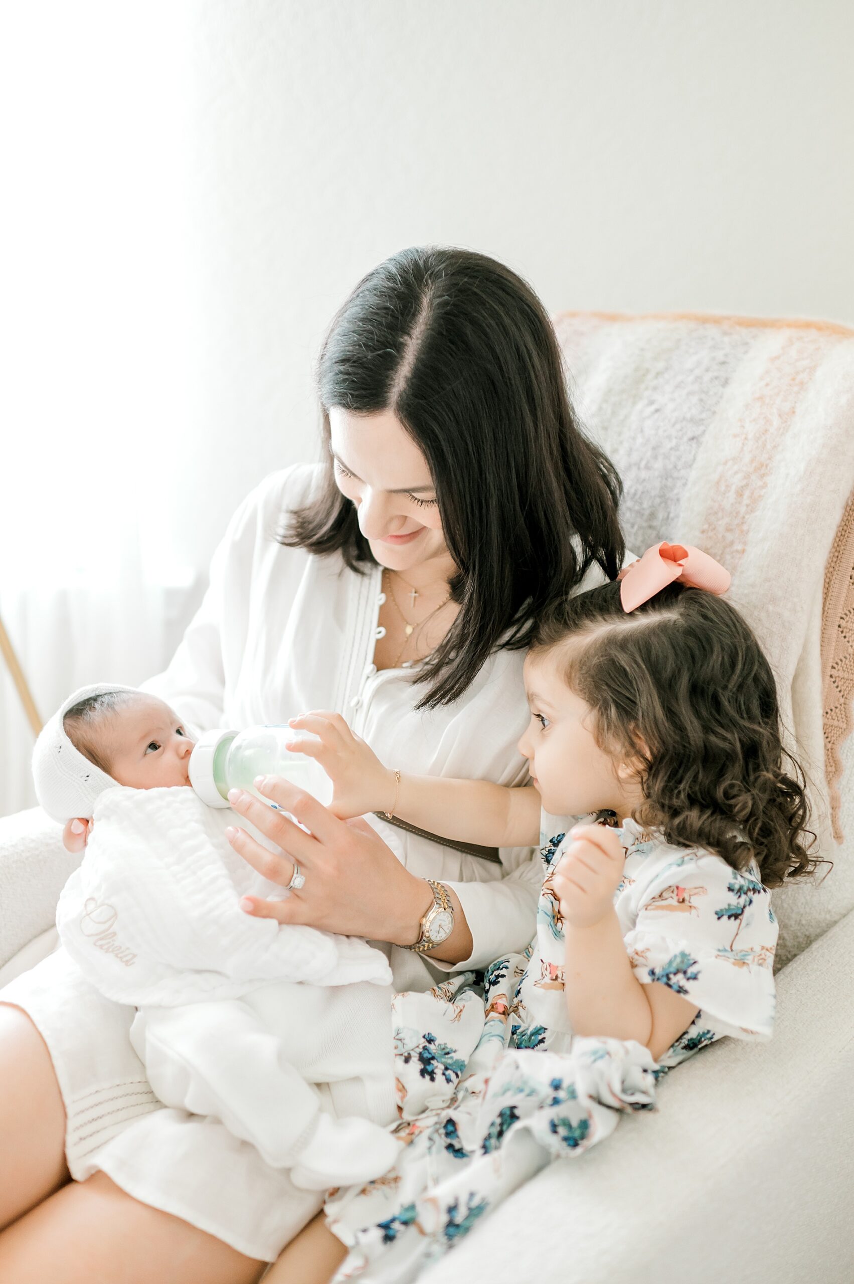 mom feeds newborn girl with toddler's help