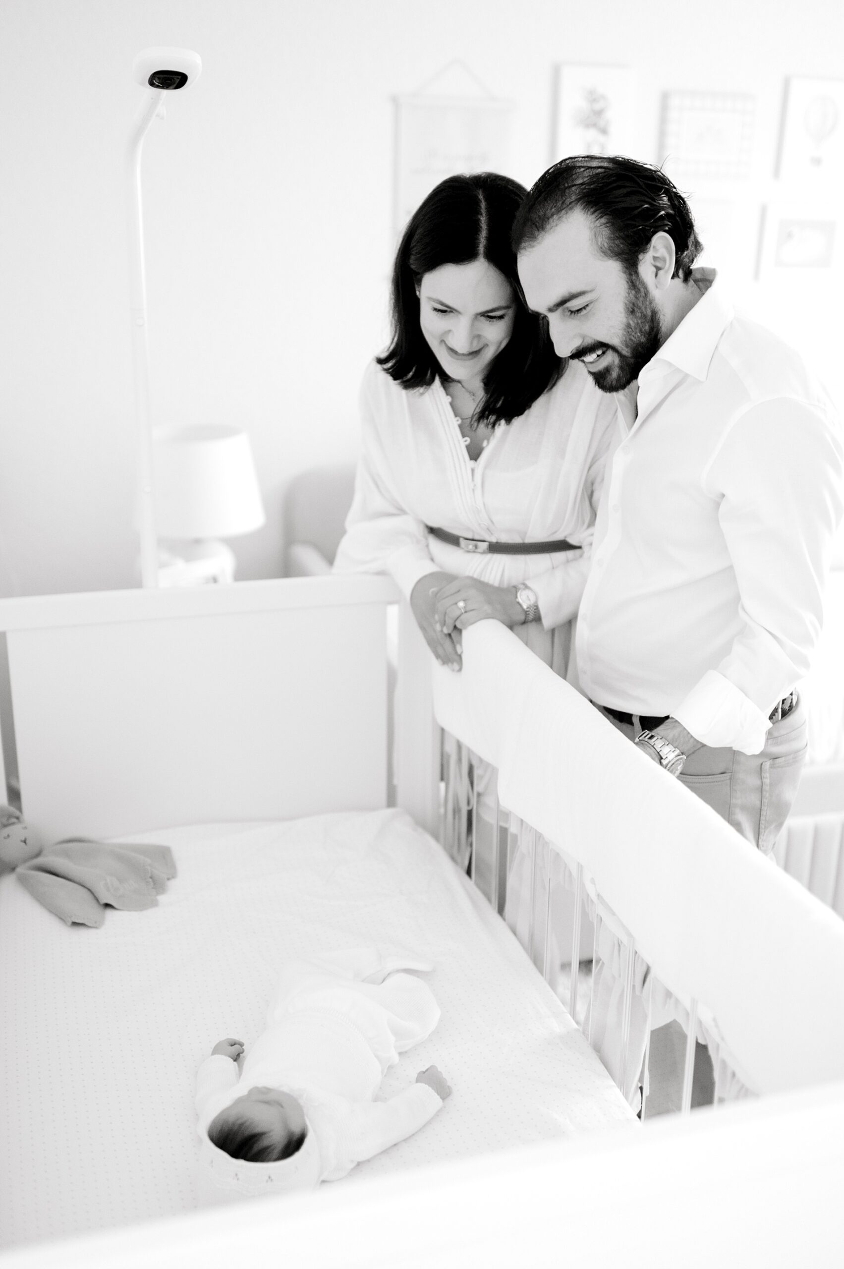 parents look down lovingly at newborn sleeping in crib during San Antonio, TX in-home newborn session