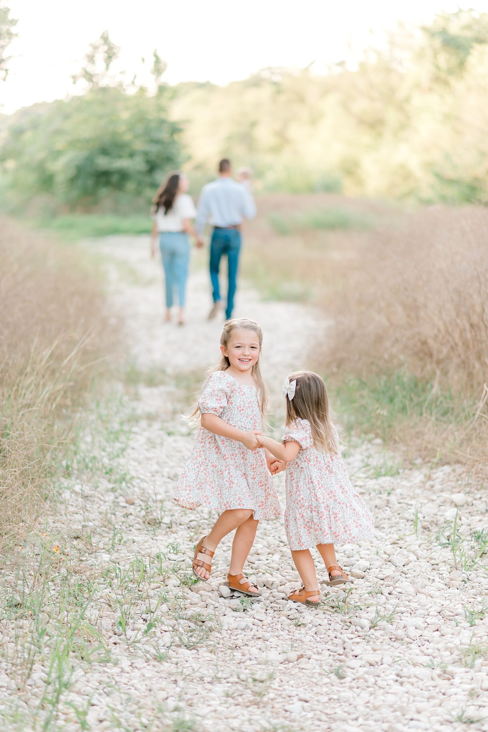 sisters play and twirl as parents walk together holding baby boy