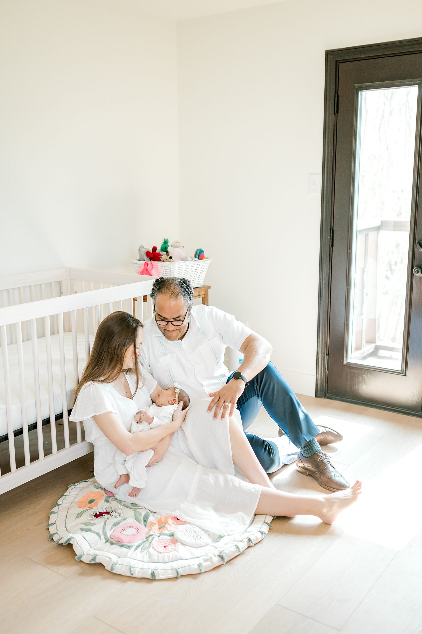 new parents sit on nursery floor holding their baby girl
