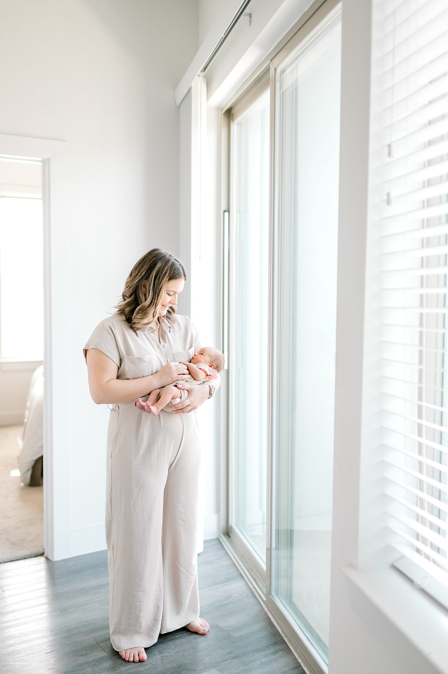 mom holds newborn by window during in home newborn session