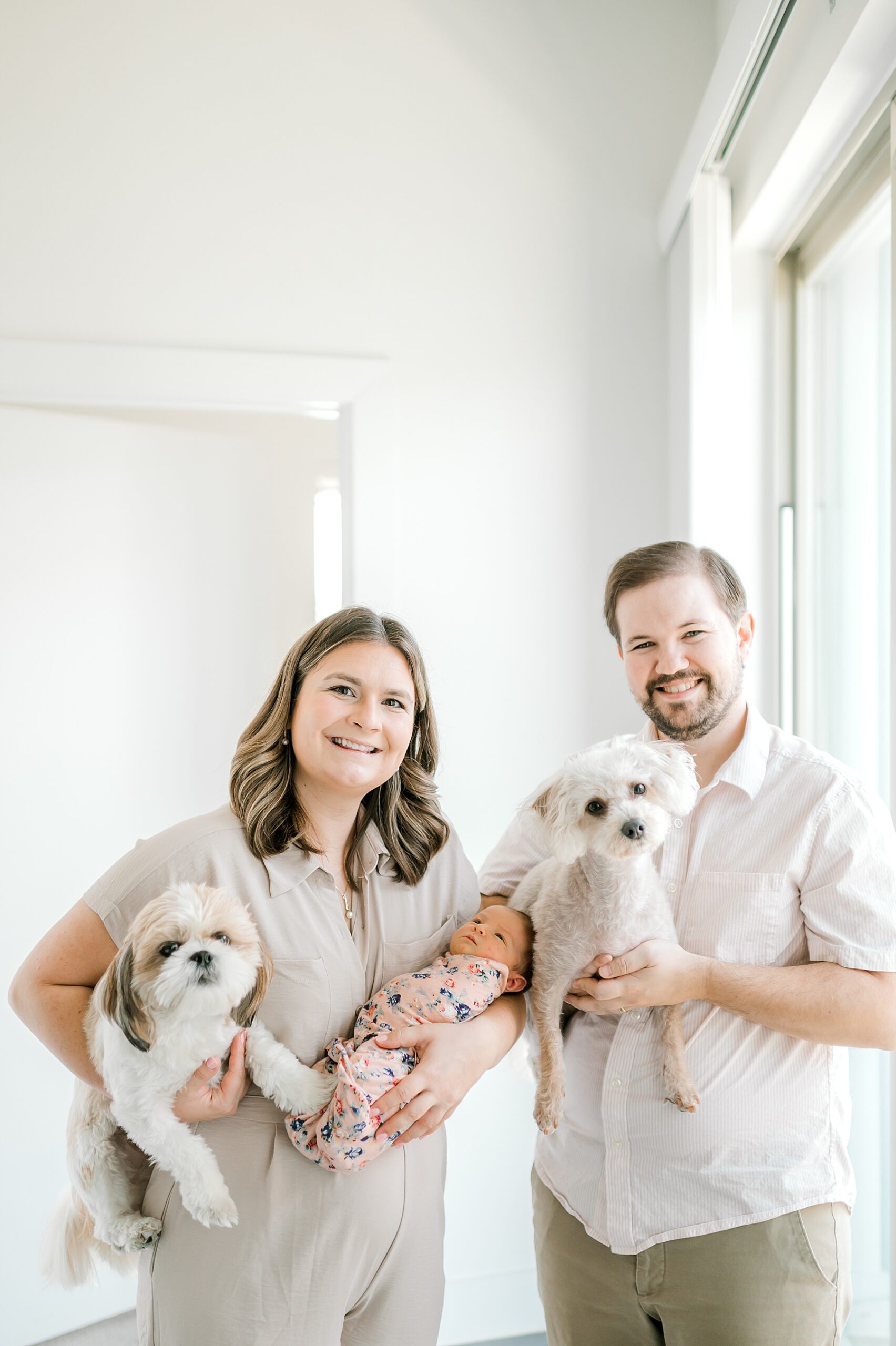parents hold newborn girl and two dogs in arms