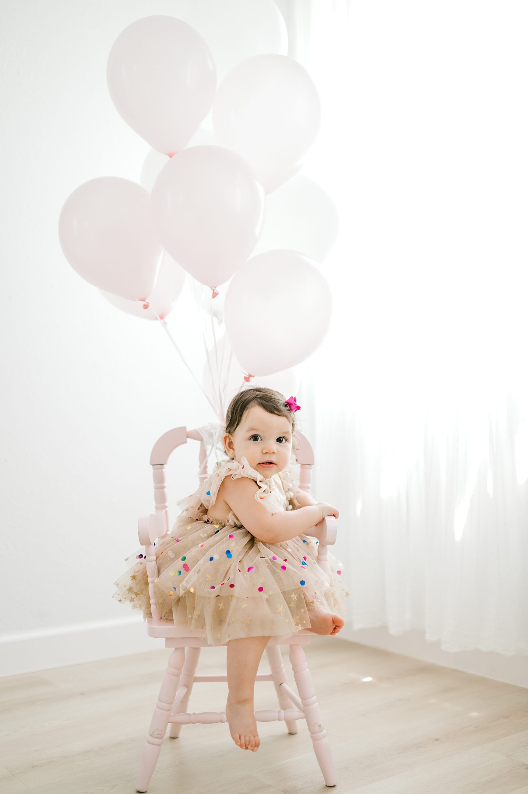 one-year old girl sits in chair with balloons