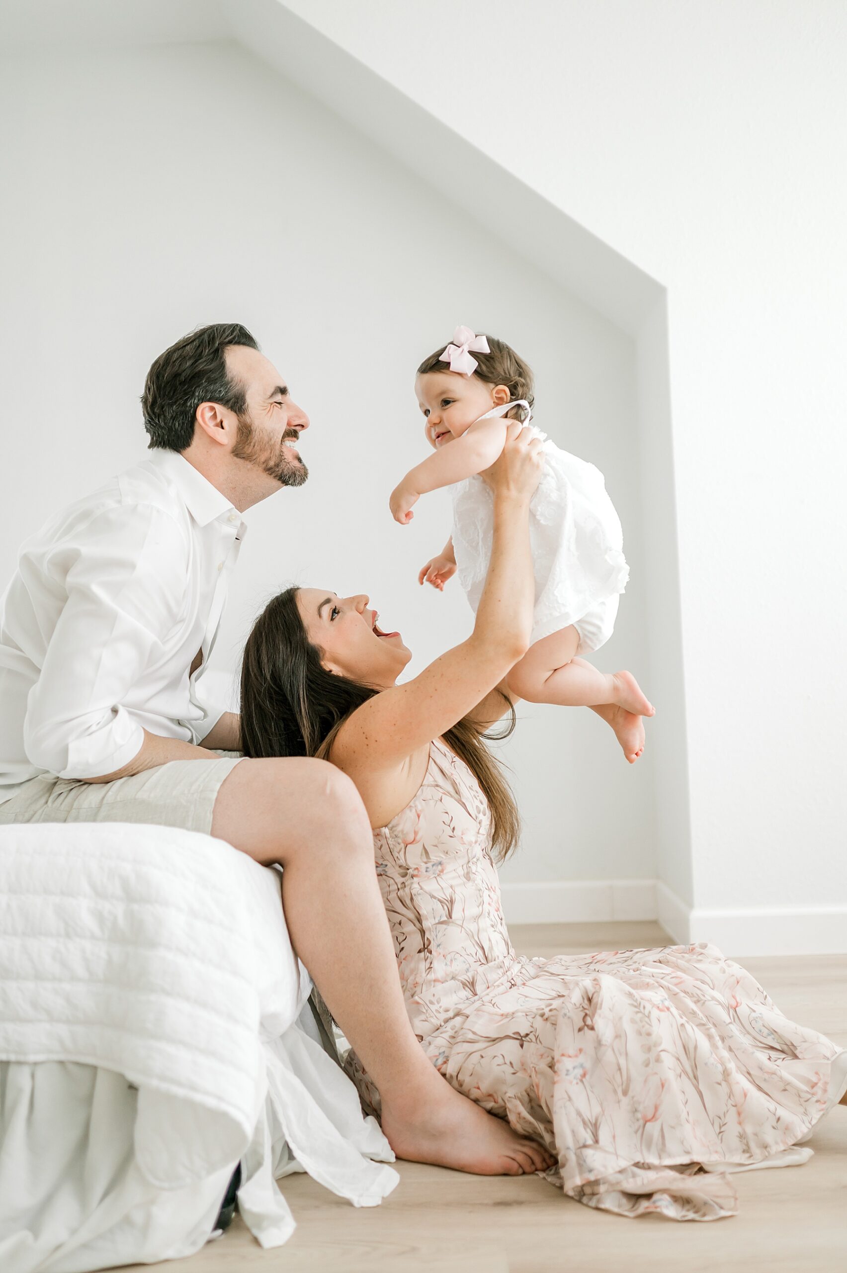 candid photo of mom holding one year old girl up in the air