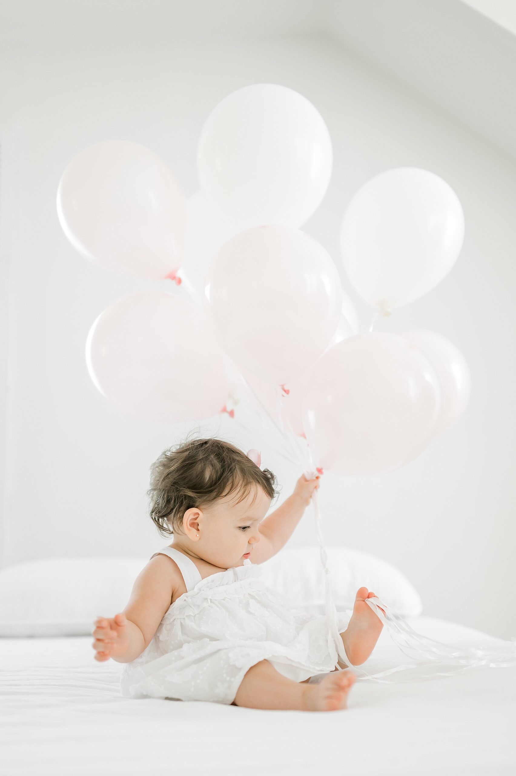 one year old girl in white dress plays with a bunch of balloons