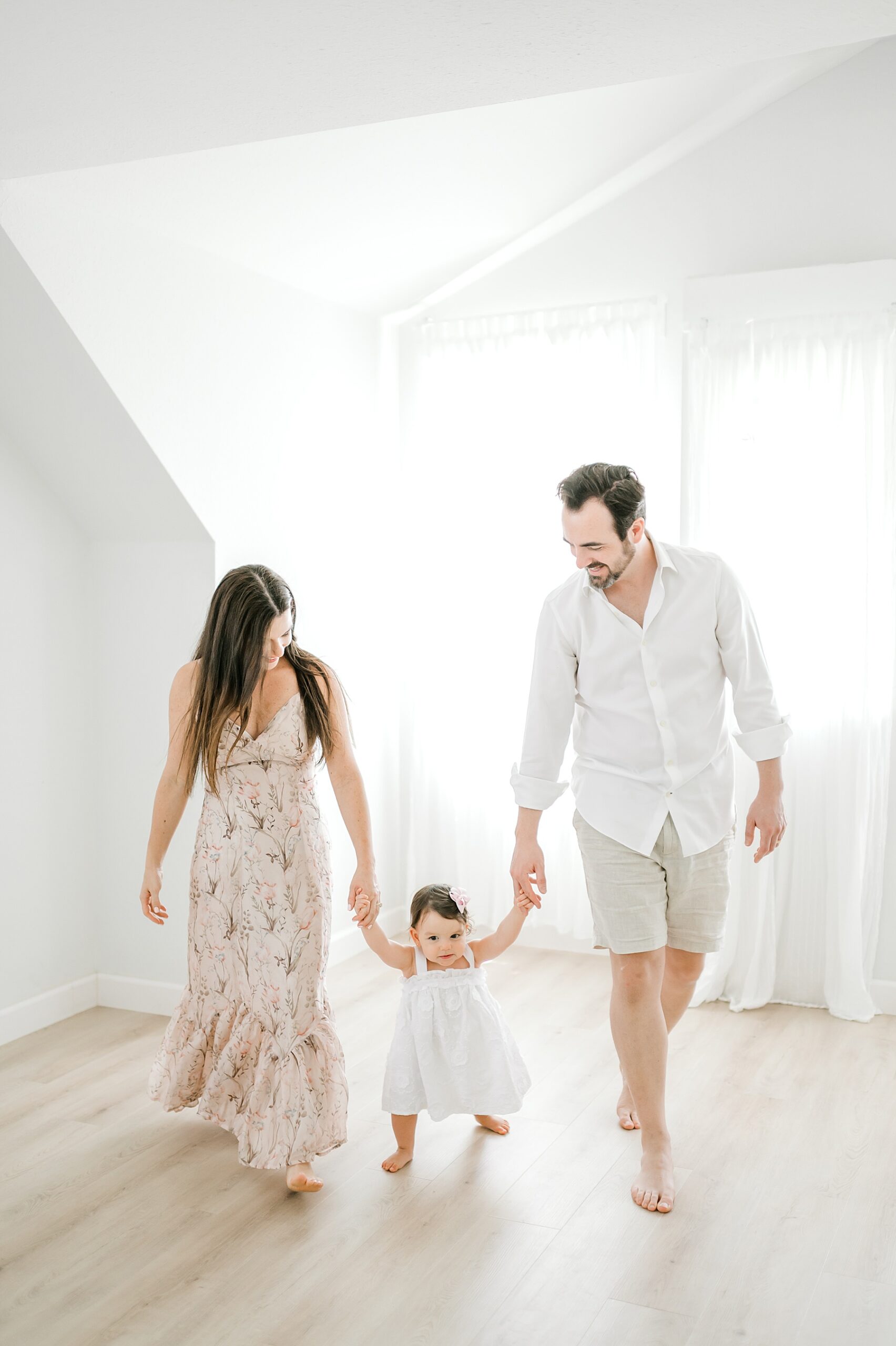 parents hold little girl's hands and help her walk