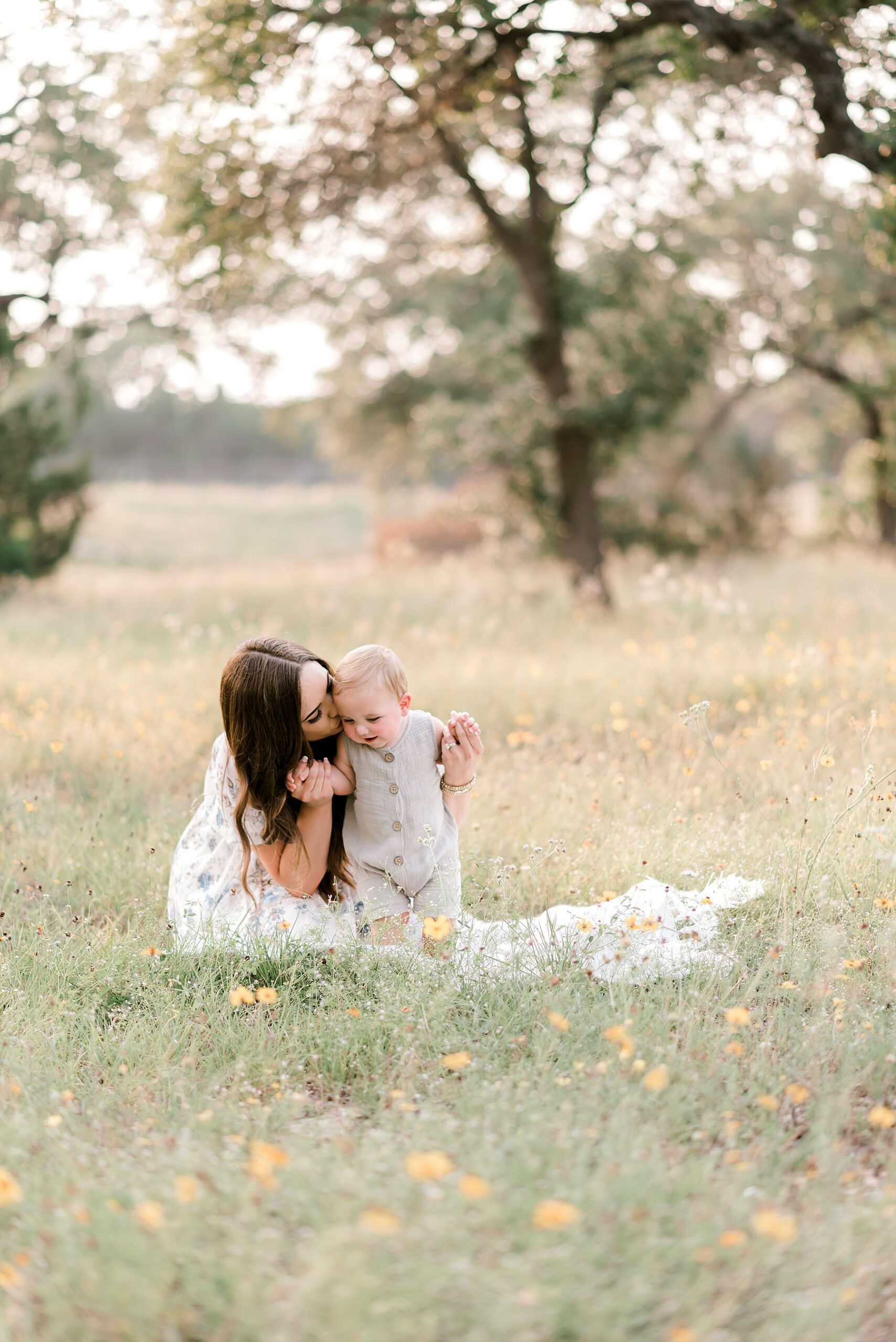 mom sits with baby boy in field of flowers
