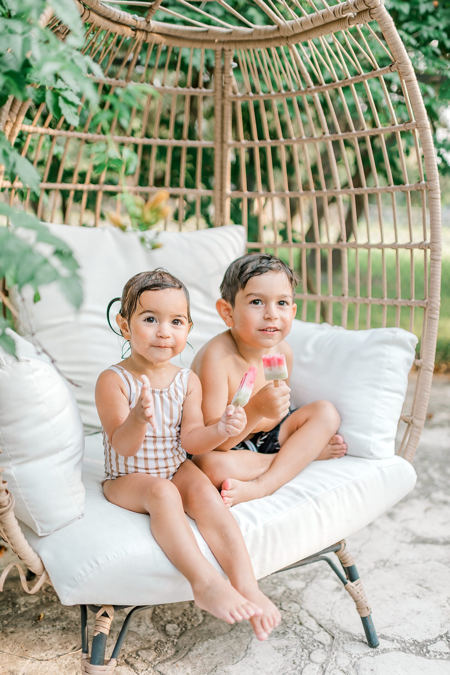 two kids sit outside eating a popsicle