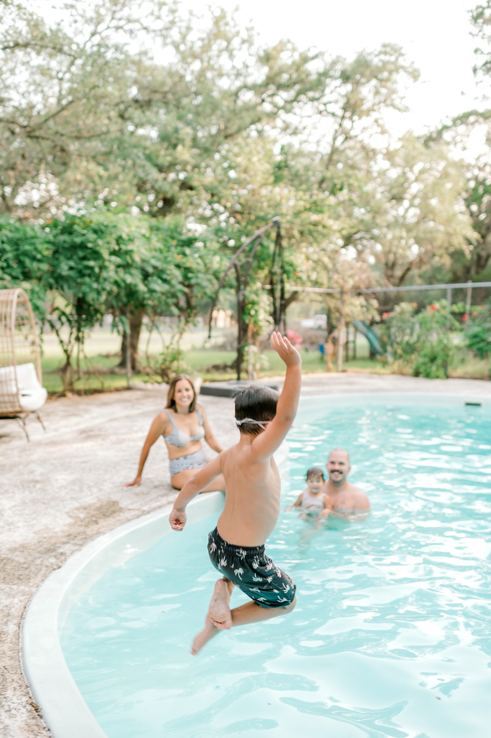 boy jumps in pool with family during Backyard Pool Party Summer Family Session