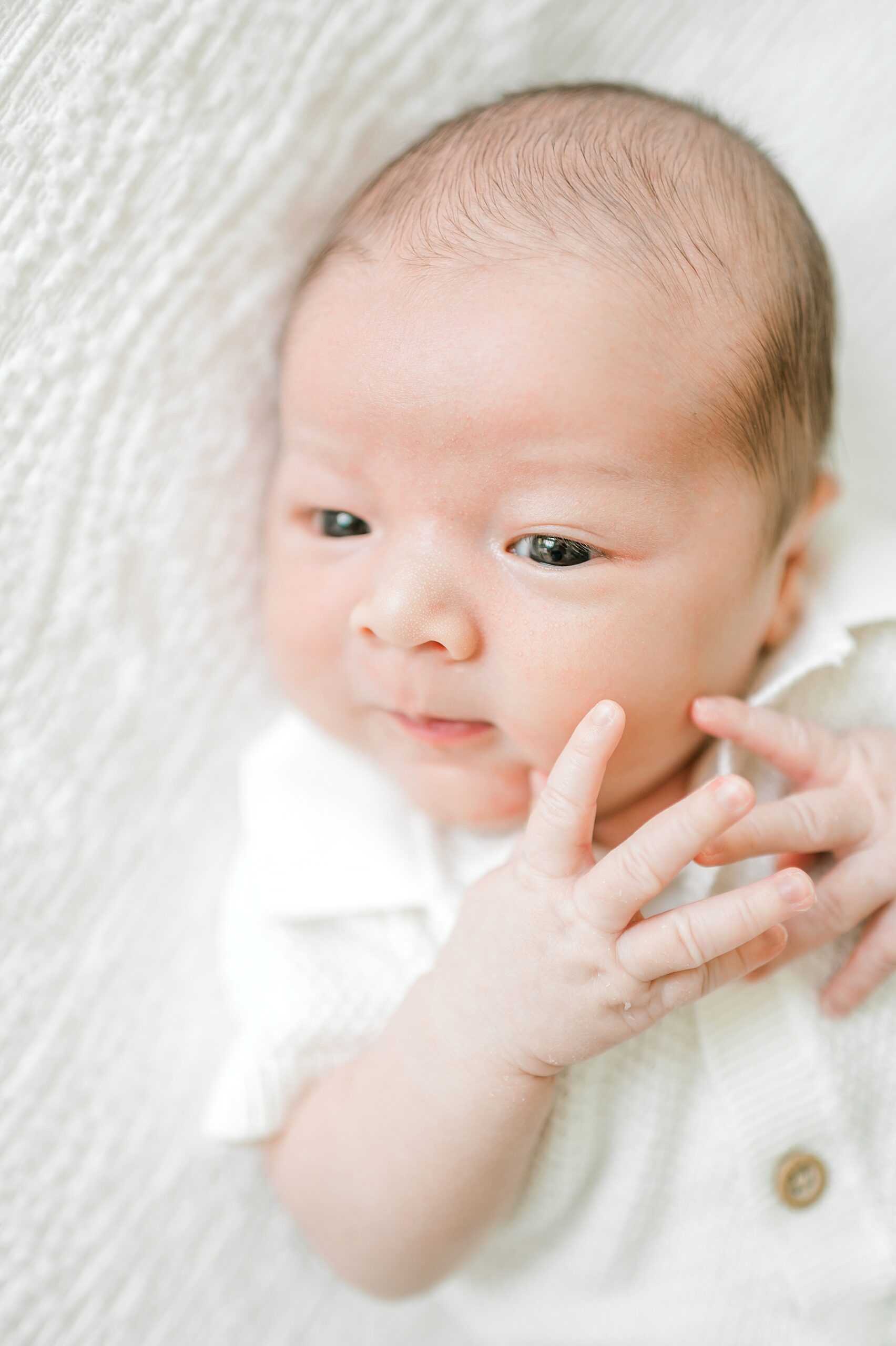 awake newborn boy in white outfit during lifestyle in-home portraits