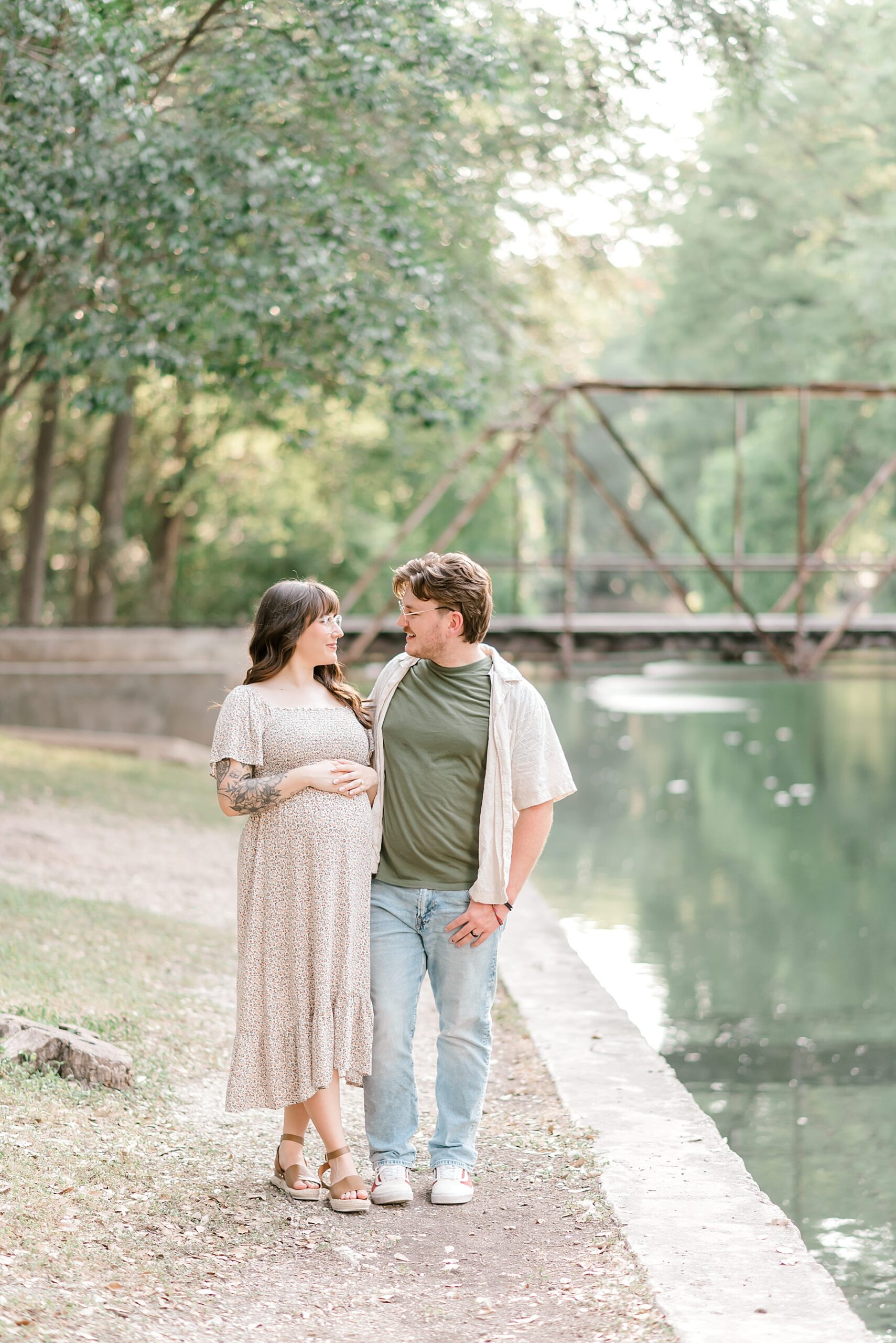 couple walk by the pond at  Brackenridge Park during maternity session