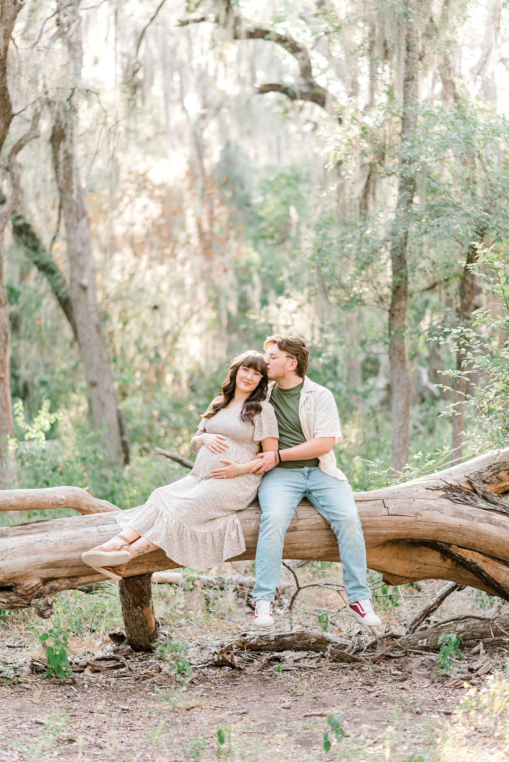 couple sitting on fallen tree during Brackenridge Park Maternity Photos 