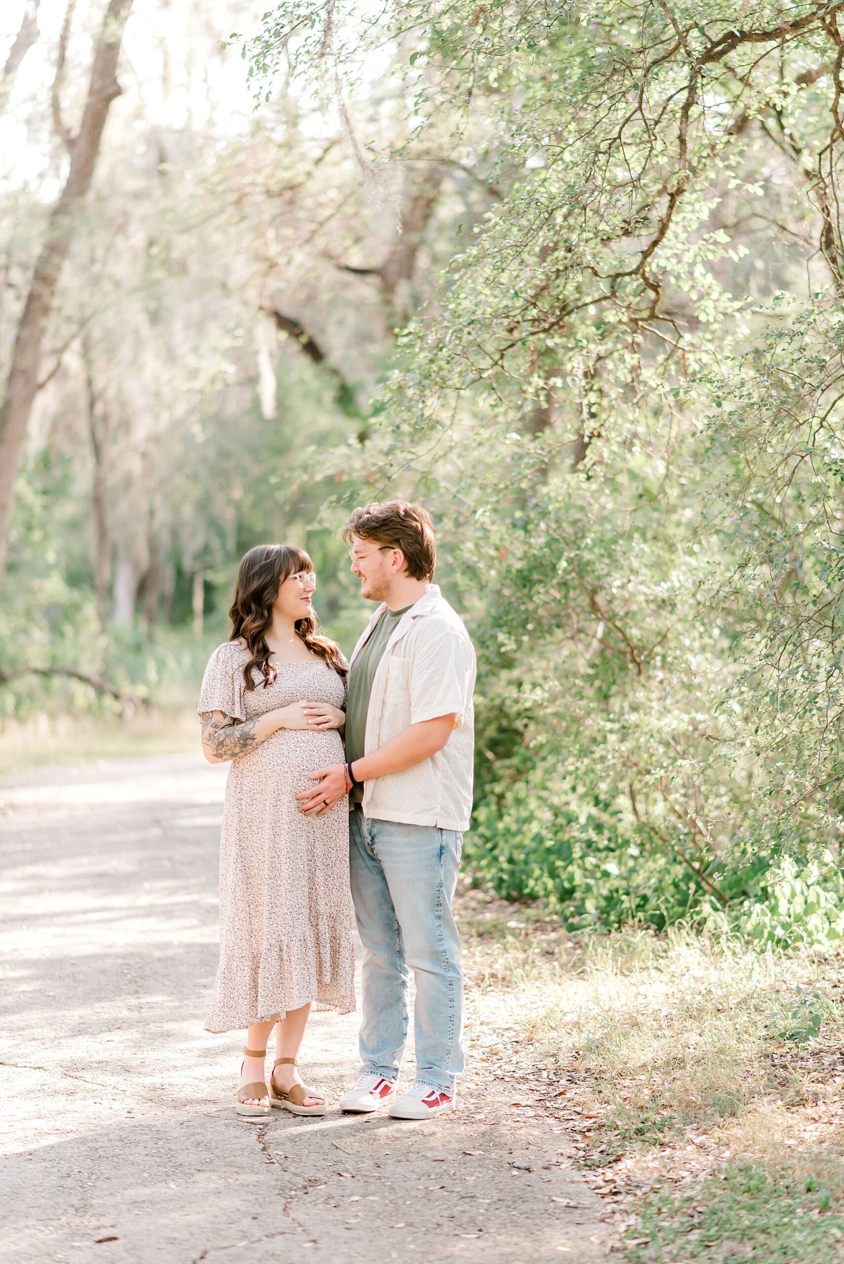 expecting parents stand in park for maternity photos 