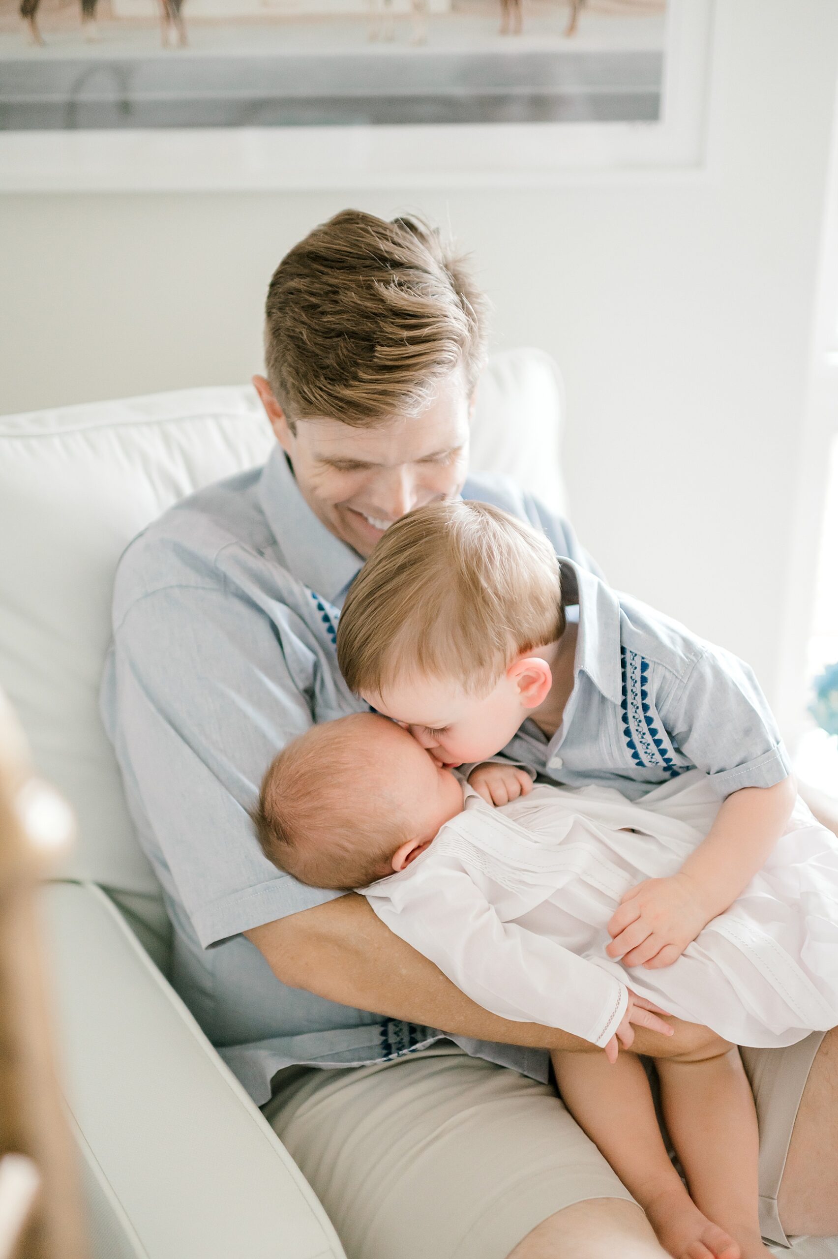 older brother kisses little brother while sitting with dad