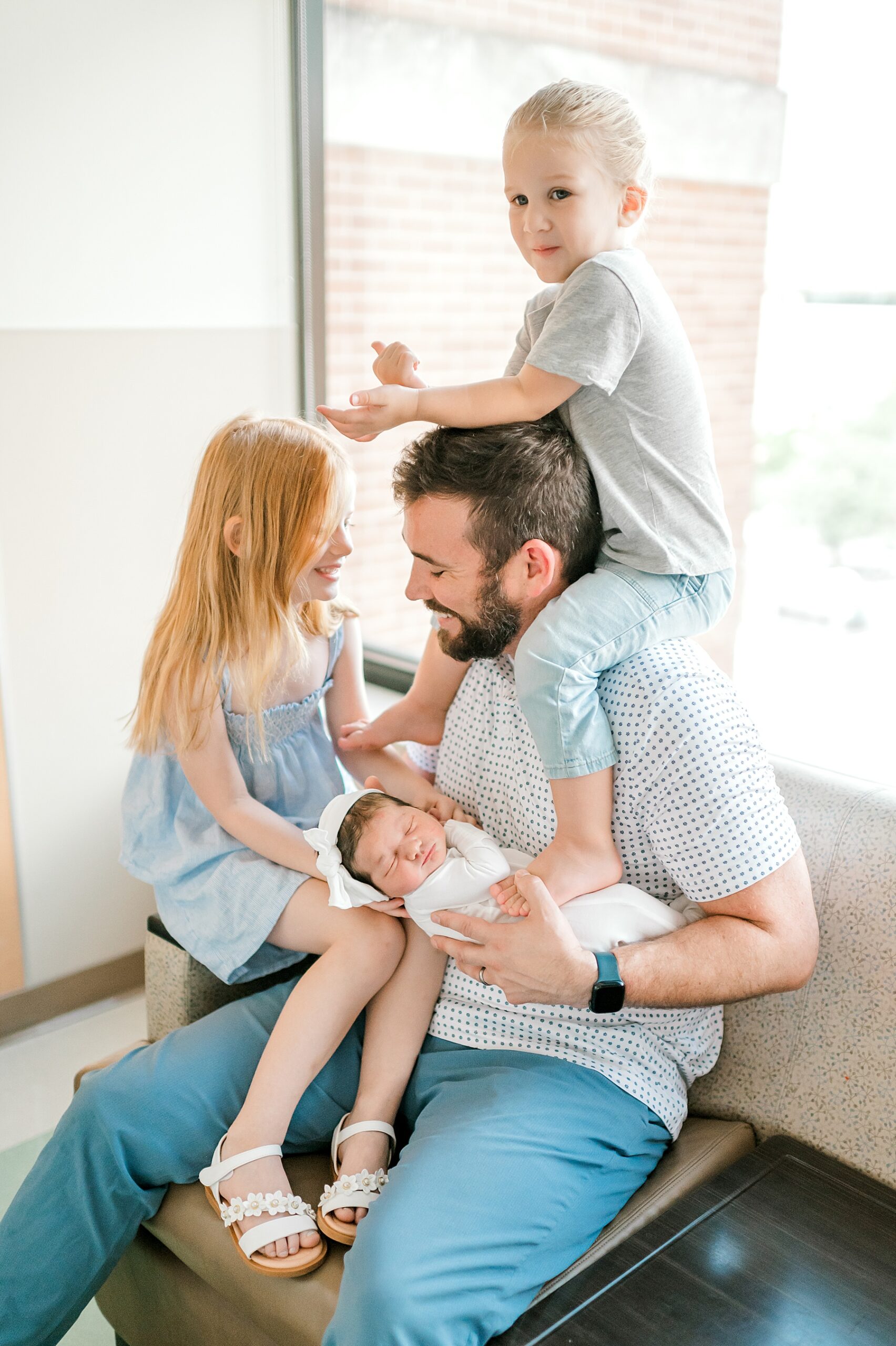 dad holds newborn with older children sitting with him 