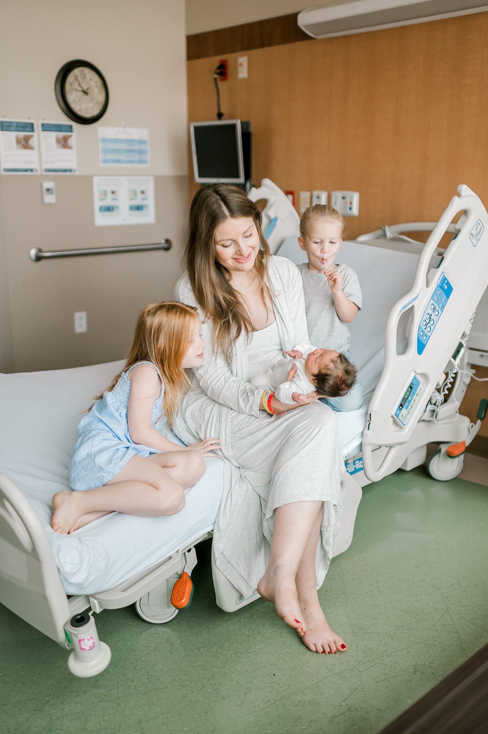 mom holds newborn on hospital bed with 2 older children nearby