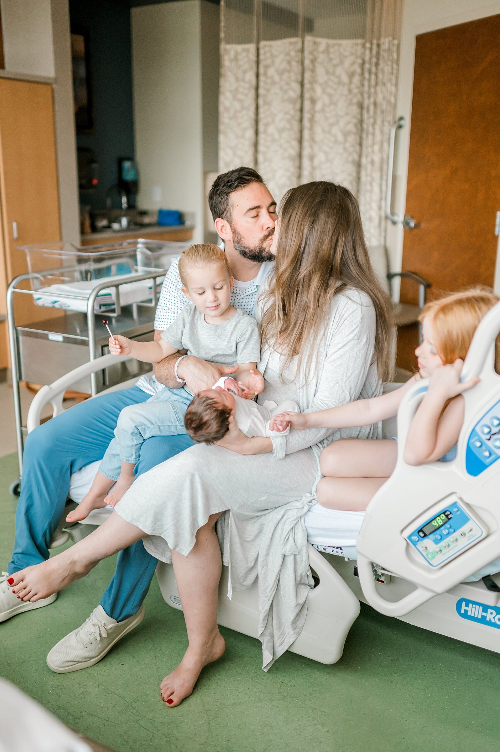 parents kiss holding their newborn with two older children sitting next to them