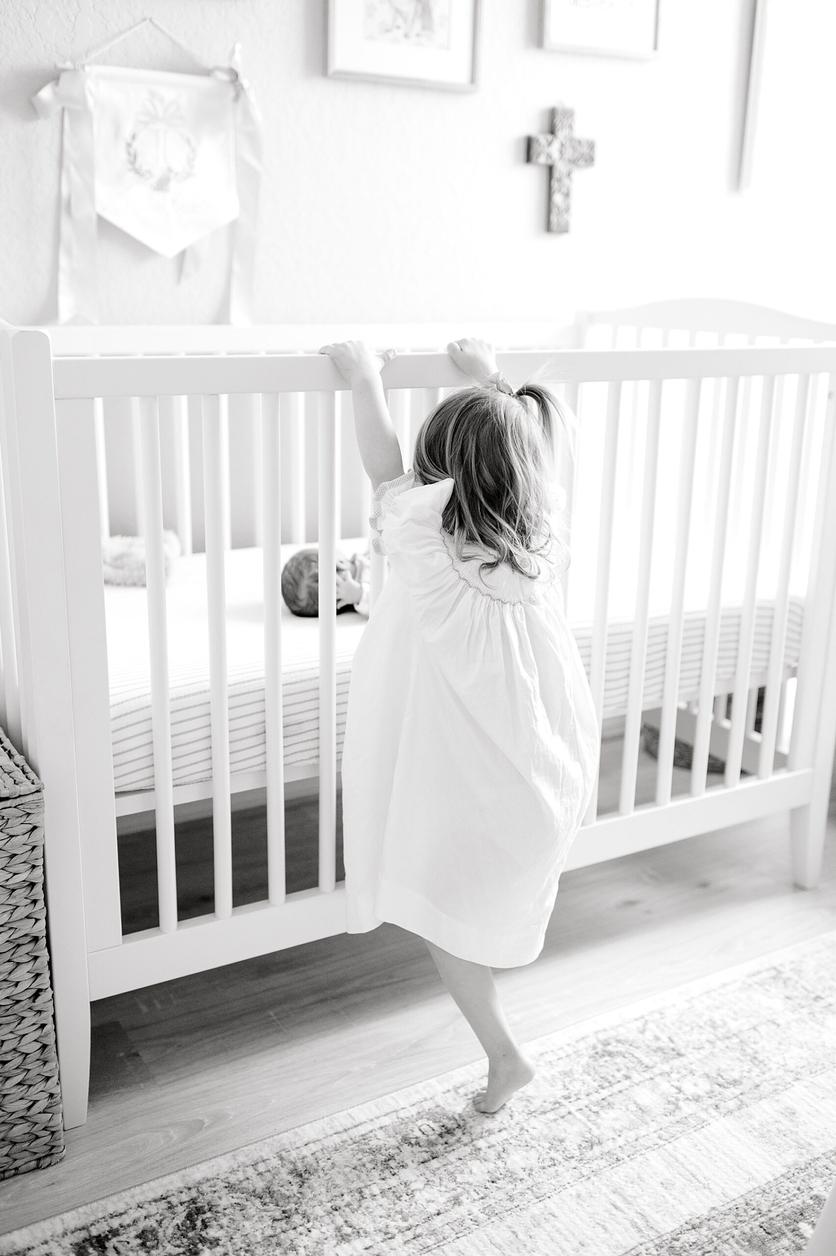 baby in crib with big sister reaching up on crib