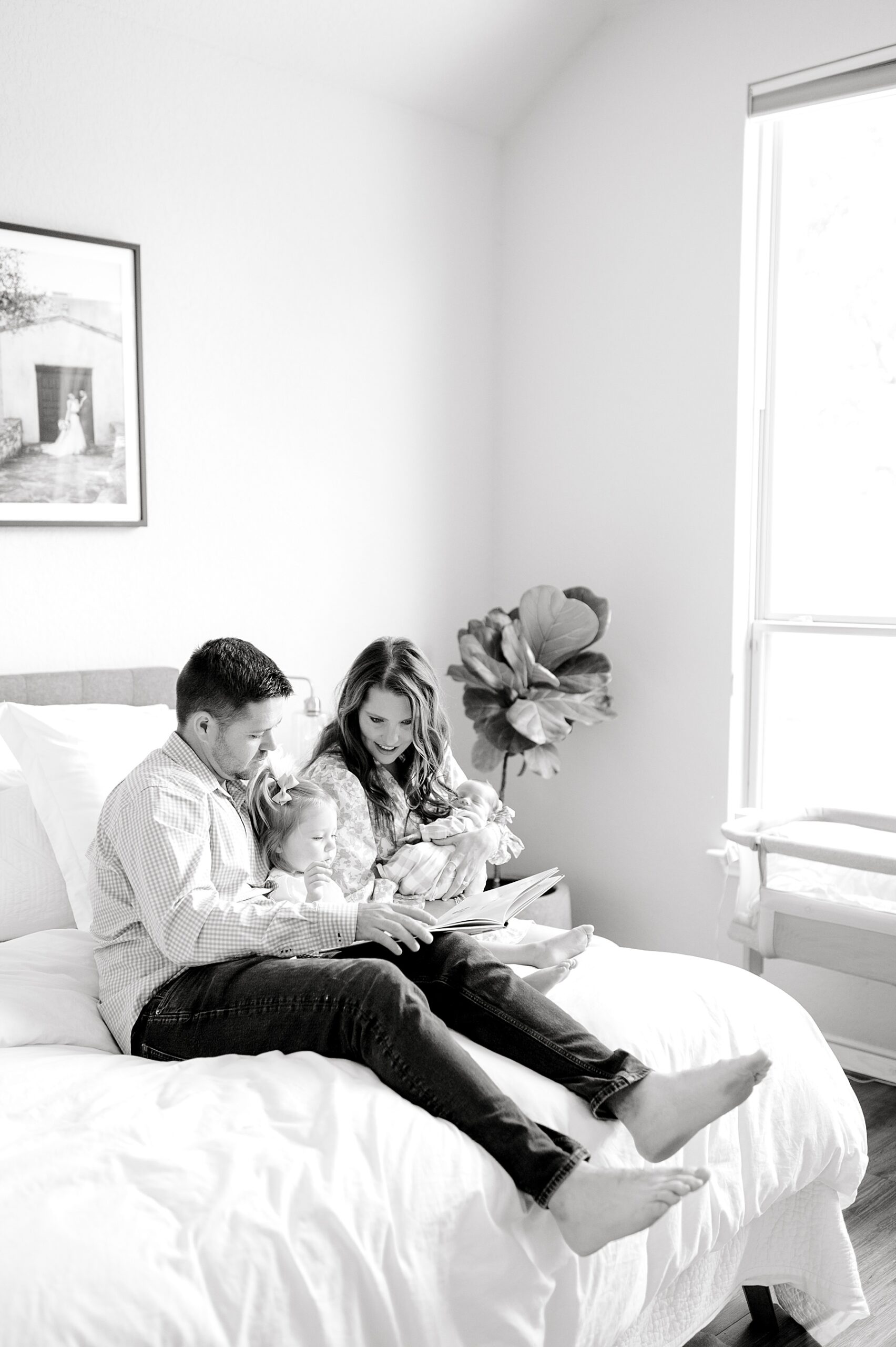 parents hold newborn and big sister while they sit together on bed
